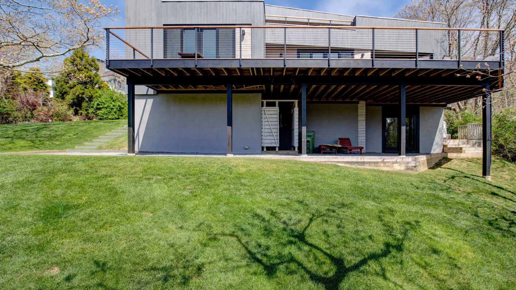 A modern house stands beyond a broad green lawn, with an elevated balcony.