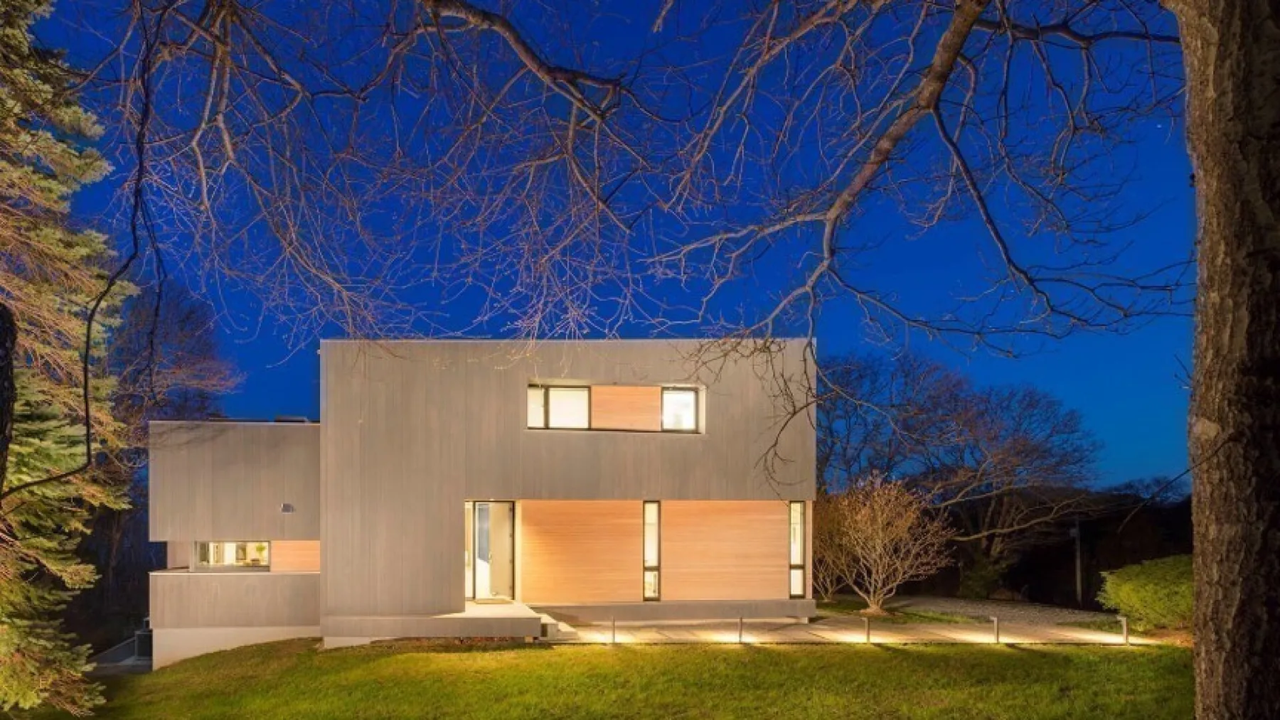 Una casa moderna al anochecer, con luces cálidas brillando en sus ventanas.