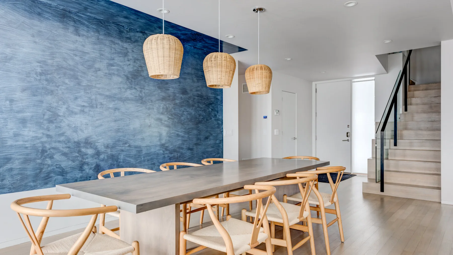 A dining area with a long table, seating, and pendant lights beside a blue wall.