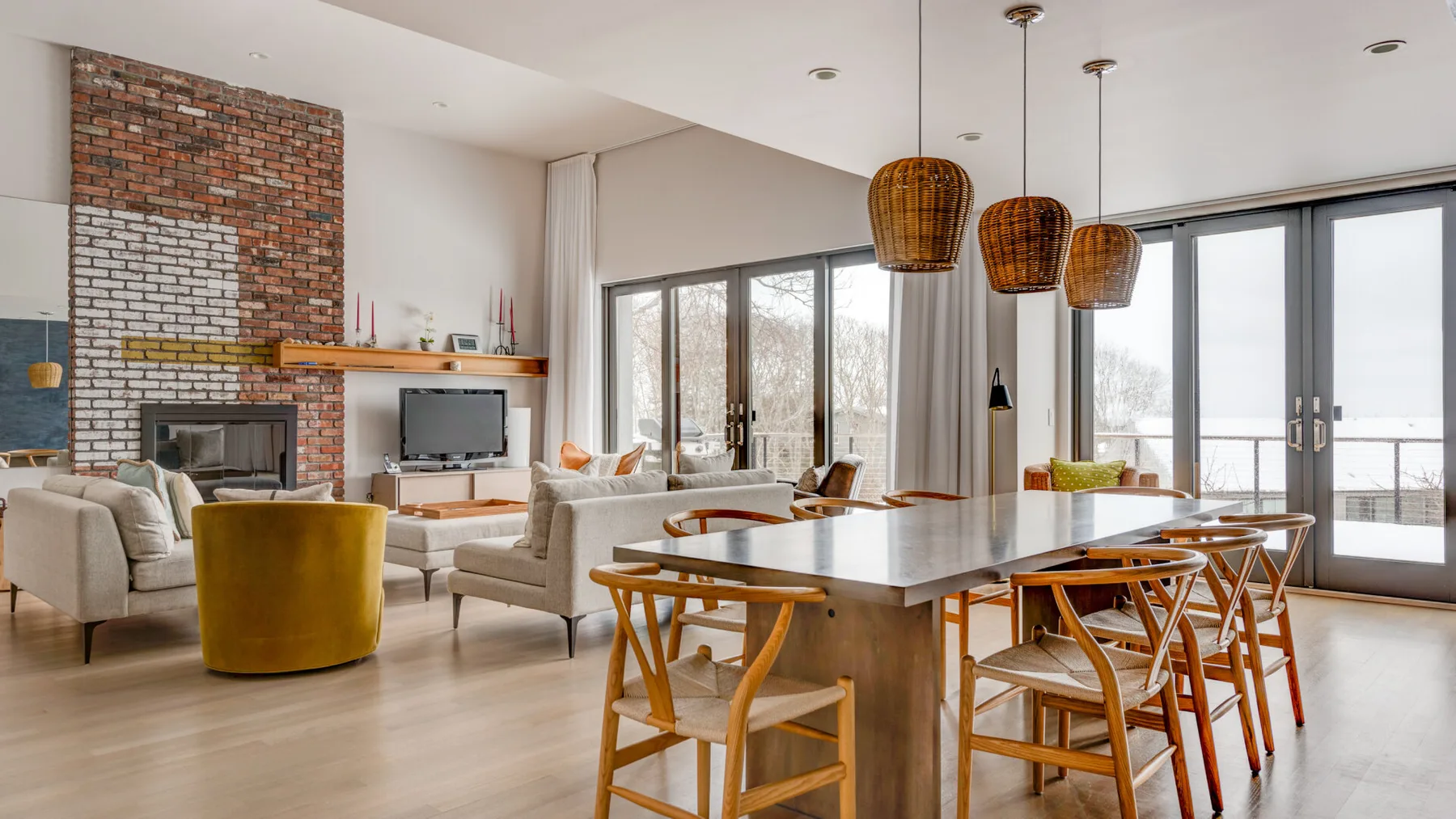 A bright open-plan living and dining area features a brick fireplace and large windows.