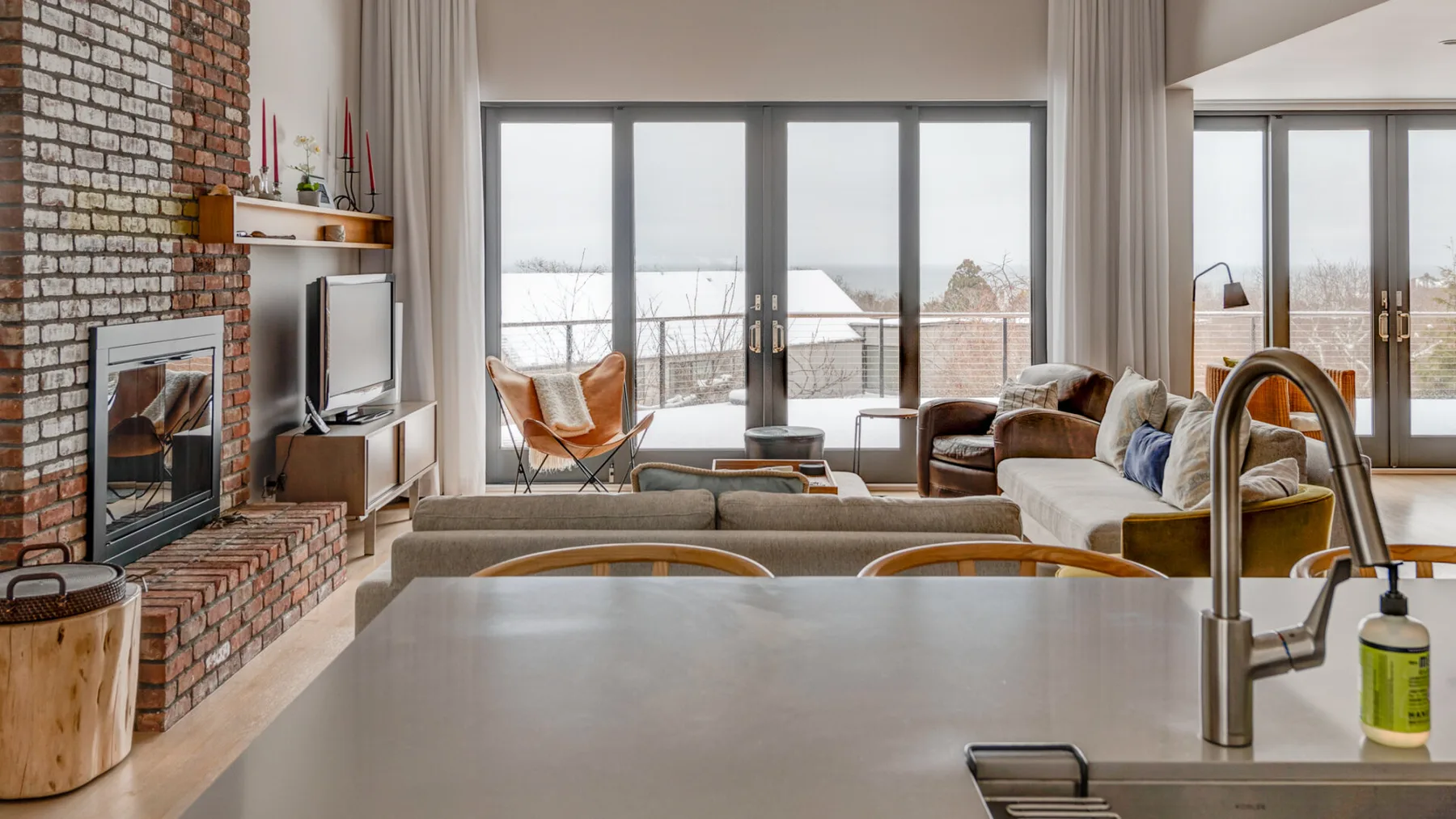 A living room opens onto a balcony through large glass doors, with a kitchen counter in front.