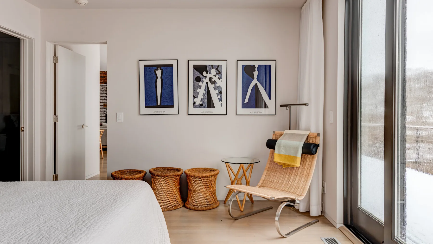 A bright bedroom with a lounge chair beside large windows and framed artwork.