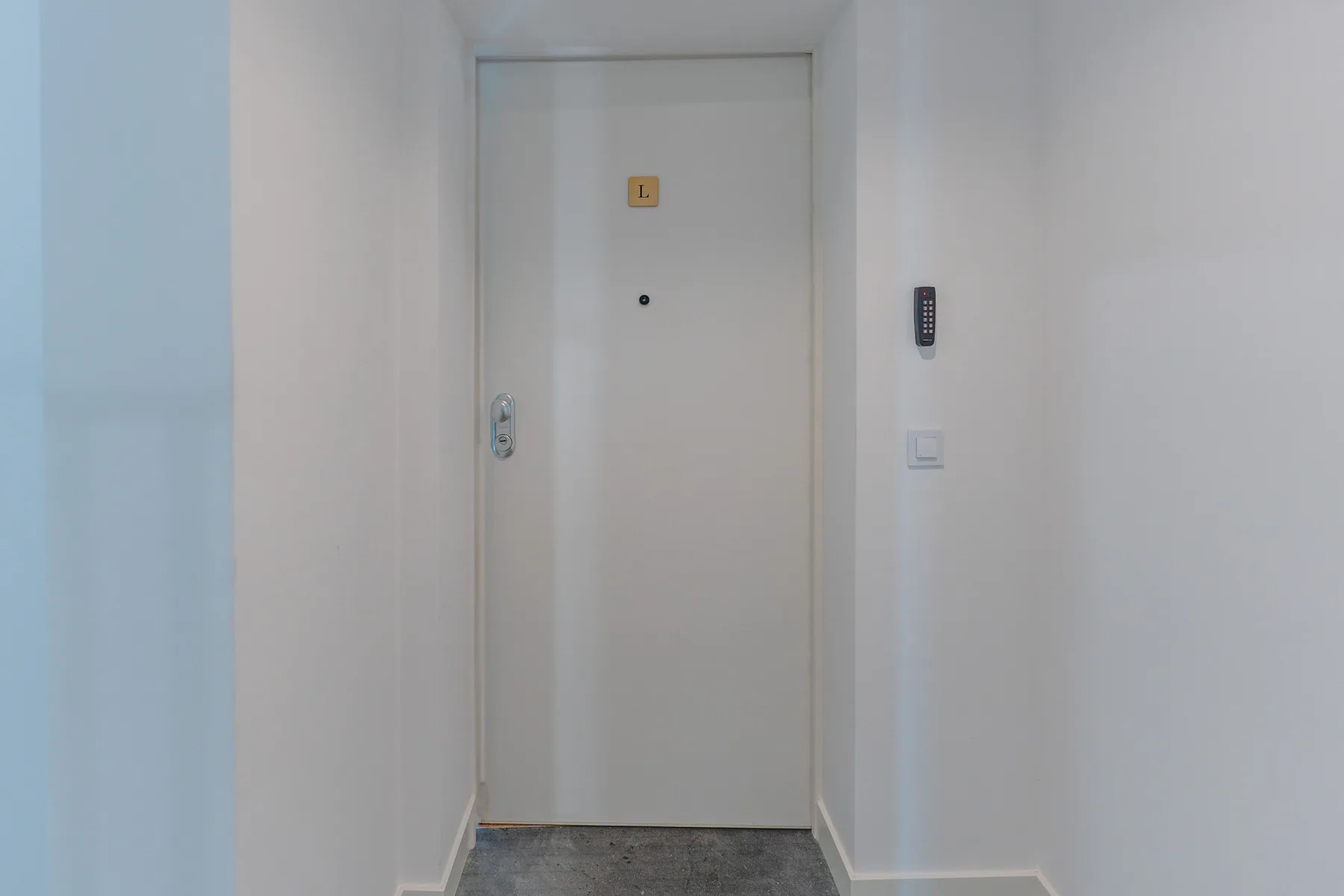 Una puerta blanca da a un pasillo corto con suelo gris.