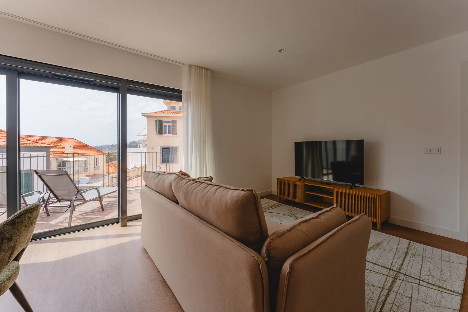Sala de estar con asientos y televisor junto a puertas corredizas de vidrio que dan a un balcón.