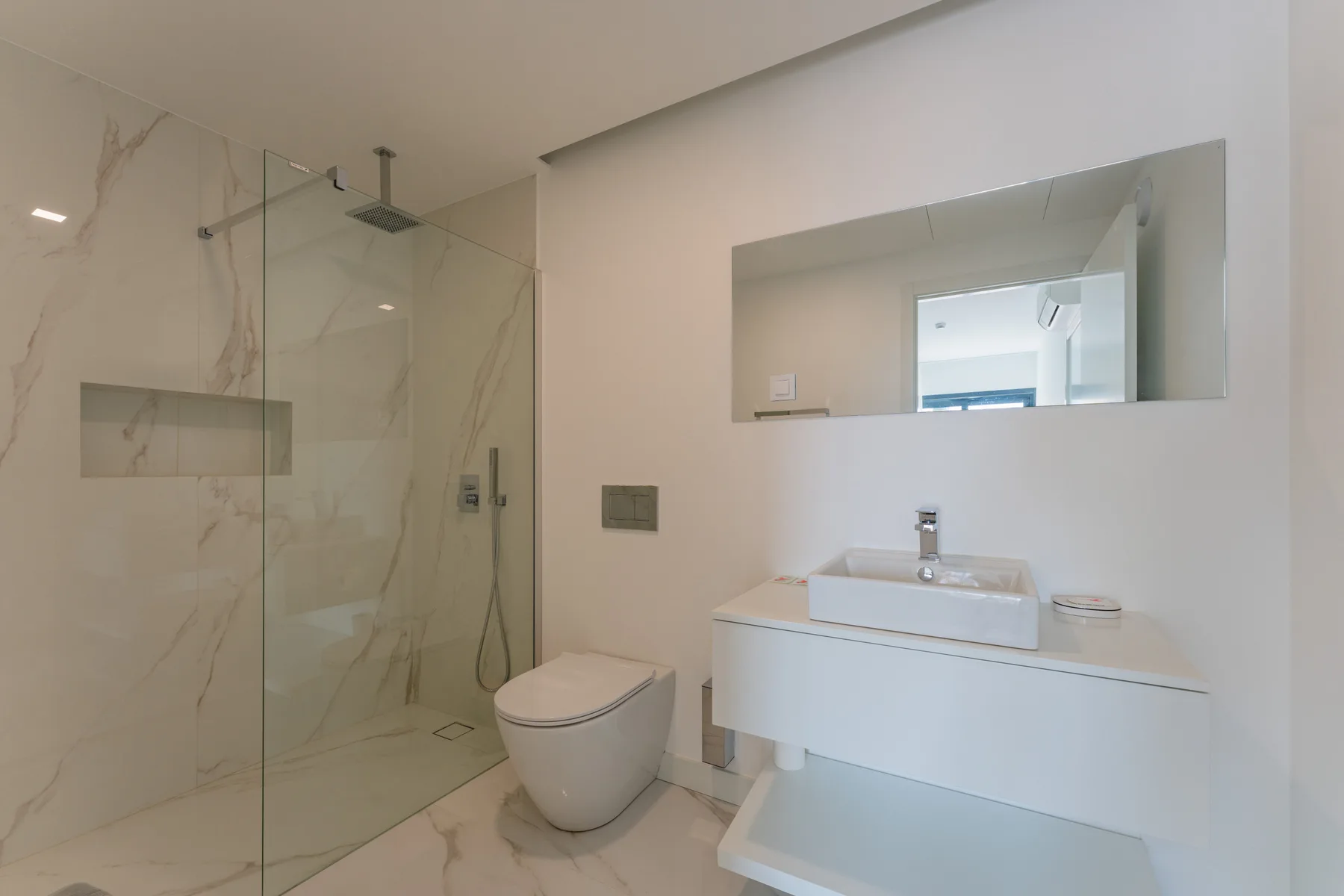 Un baño luminoso con una ducha de vidrio y un lavabo blanco.