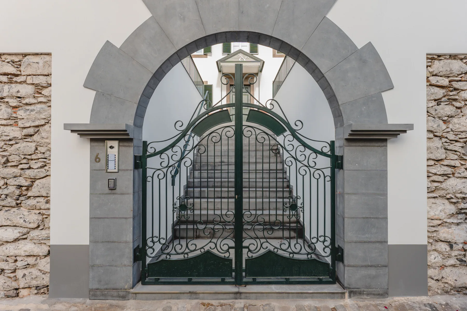 Una puerta metálica ornamentada bajo un arco de piedra da a una escalera.
