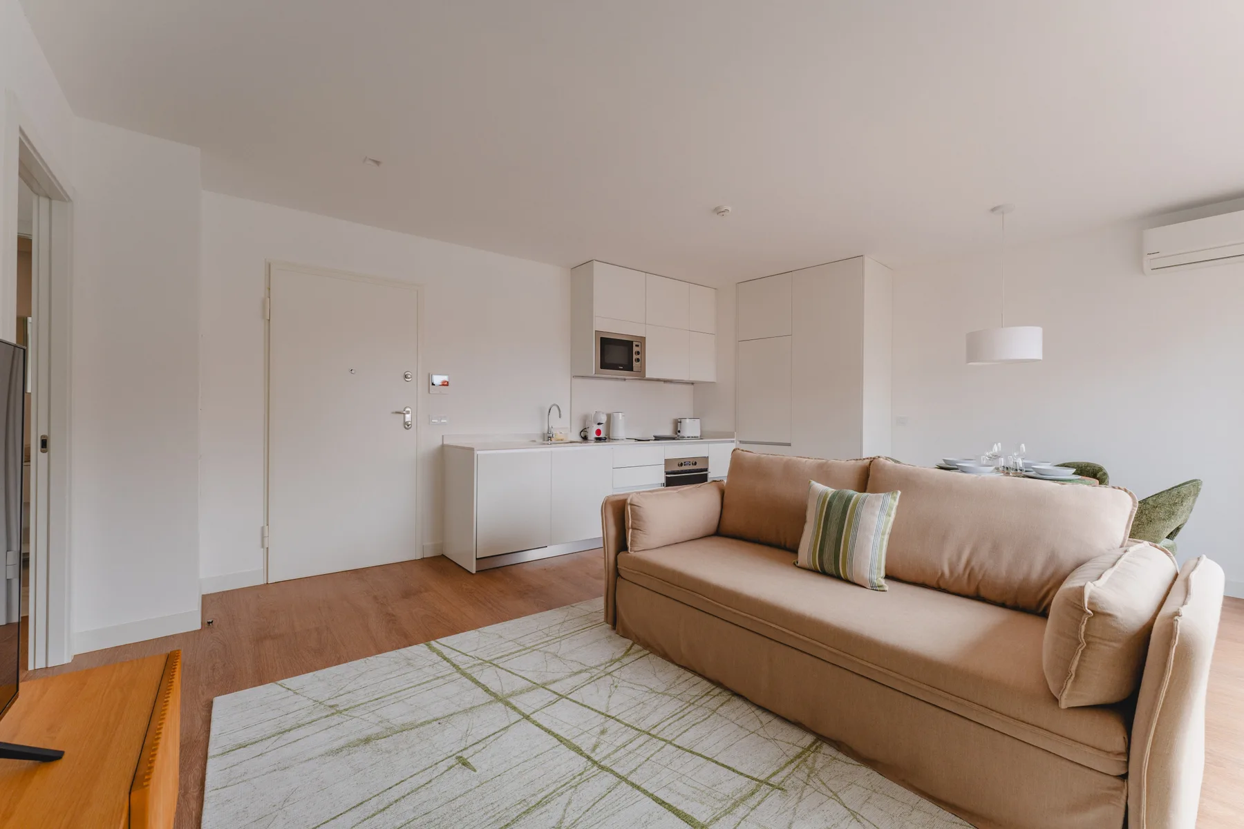 Una sala luminosa con un sofá beige junto a una cocina abierta.