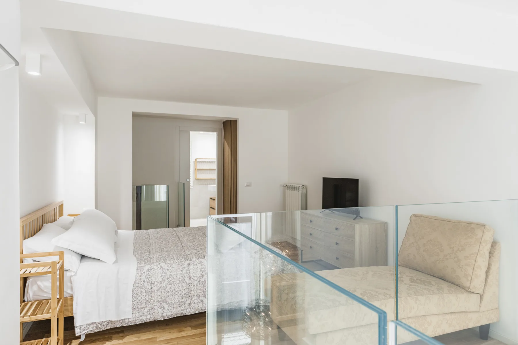 Un dormitorio luminoso con una cama y una mampara de vidrio junto a la zona de descanso.