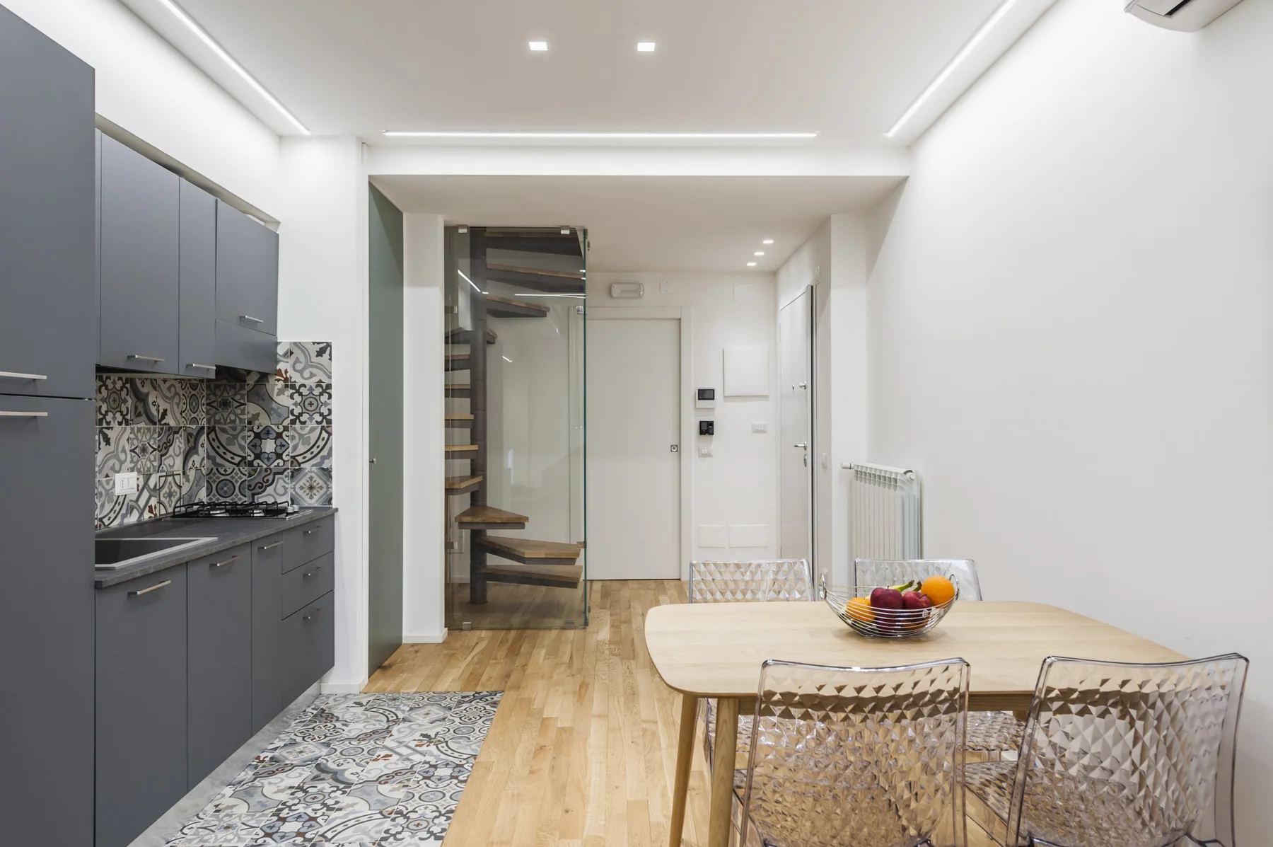 Una cocina y comedor modernos con gabinetes grises y una mesa de madera clara.
