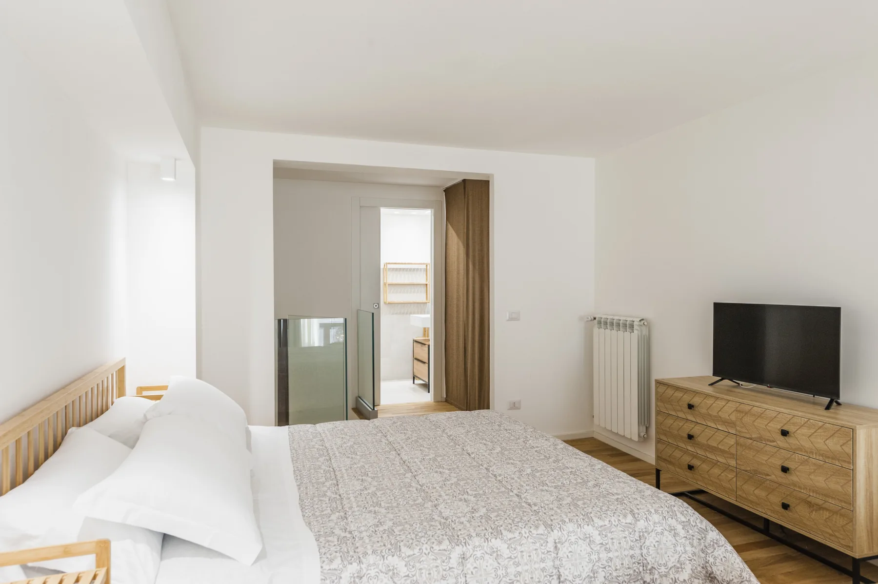 Un dormitorio luminoso con una cama, un televisor y una cómoda de madera.