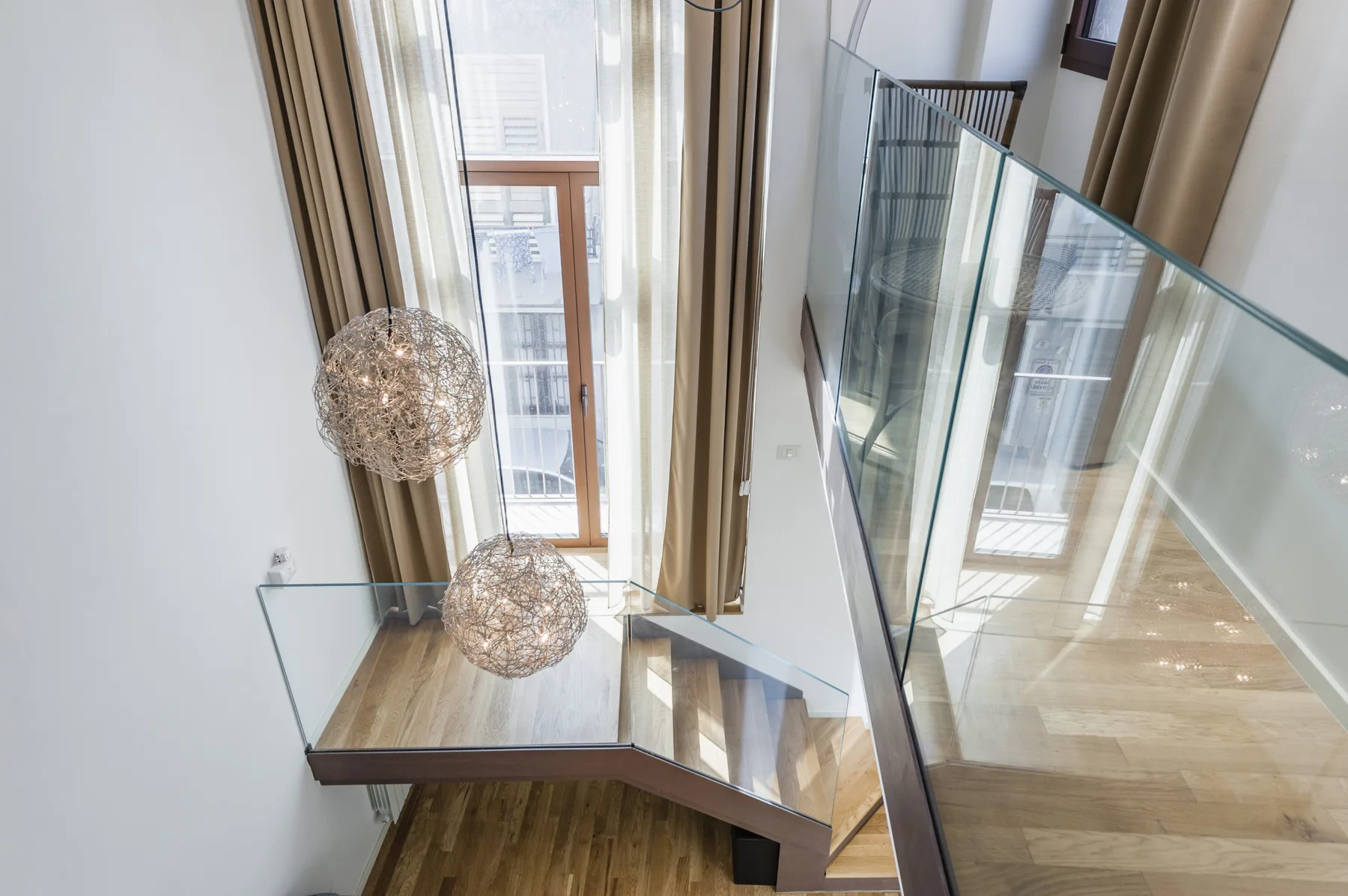 Una escalera interior luminosa con barandillas de vidrio y lámparas colgantes.