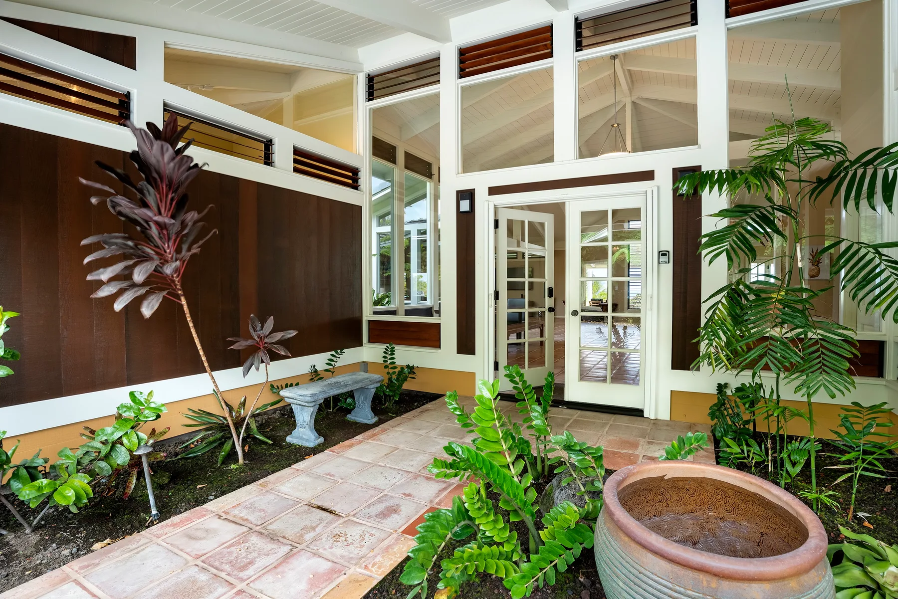 Un patio interior luminoso con plantas, un camino de baldosas y una entrada de vidrio.