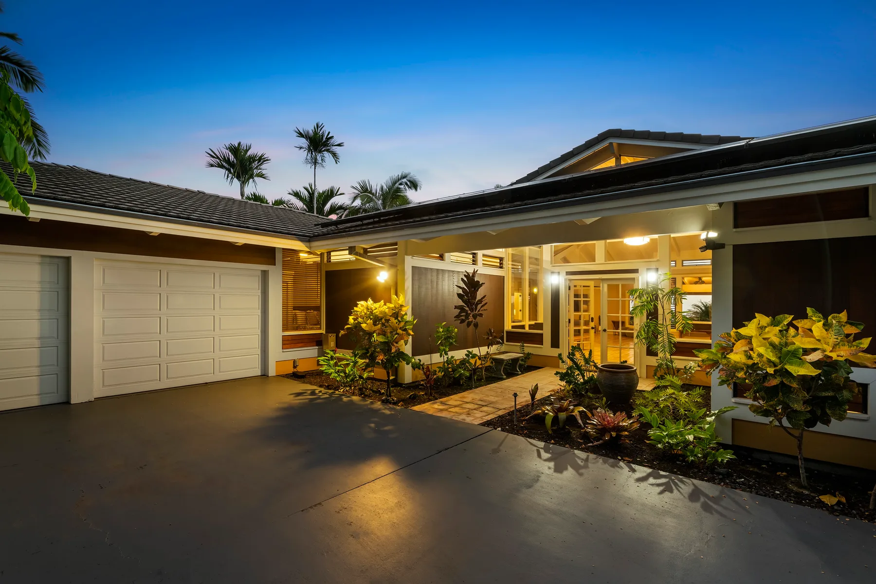 Exterior de una casa moderna con garaje, entrada iluminada y jardín con plantas.