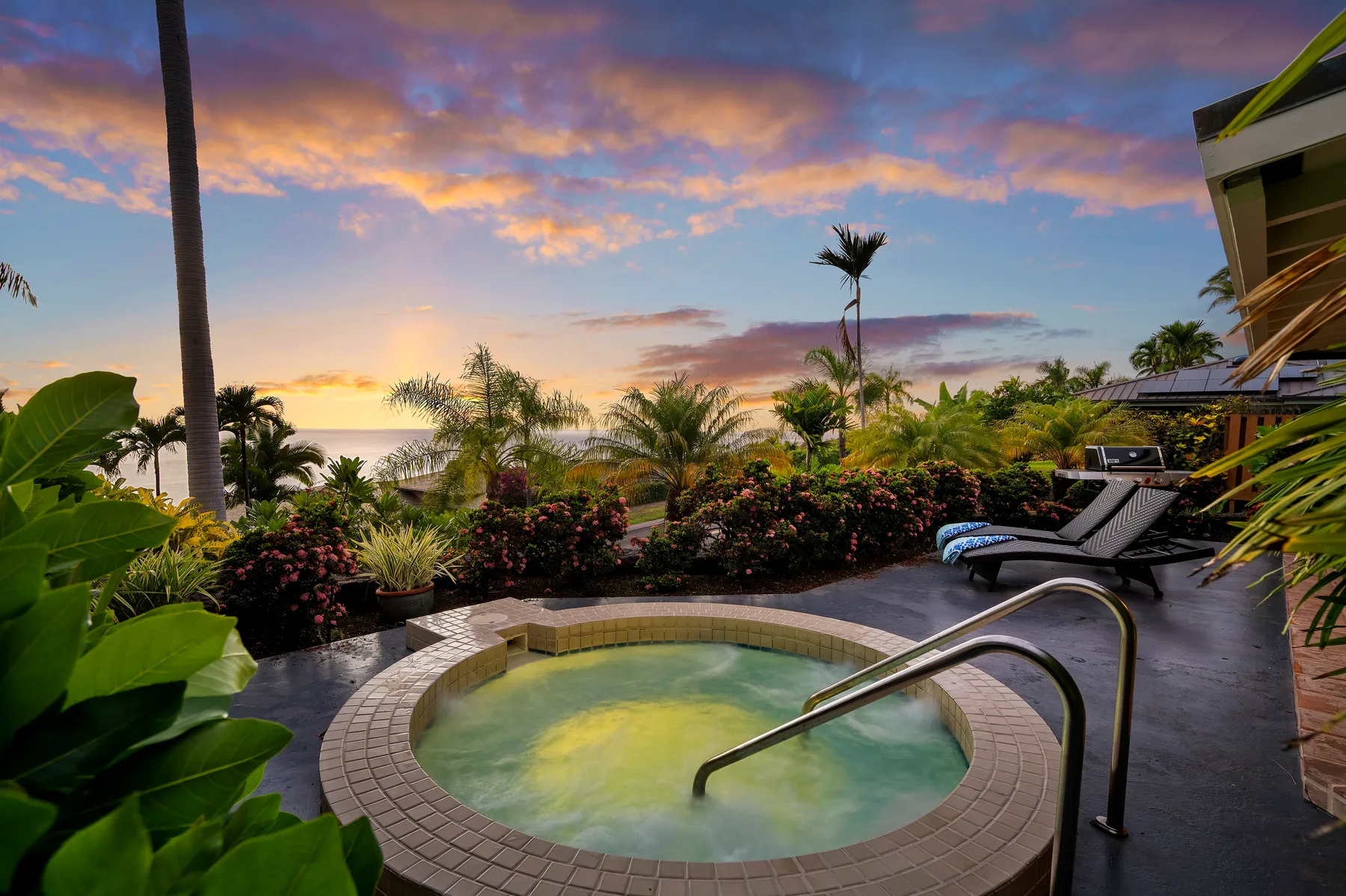 Una pequeña piscina exterior está junto a asientos de descanso y plantas tropicales al atardecer.