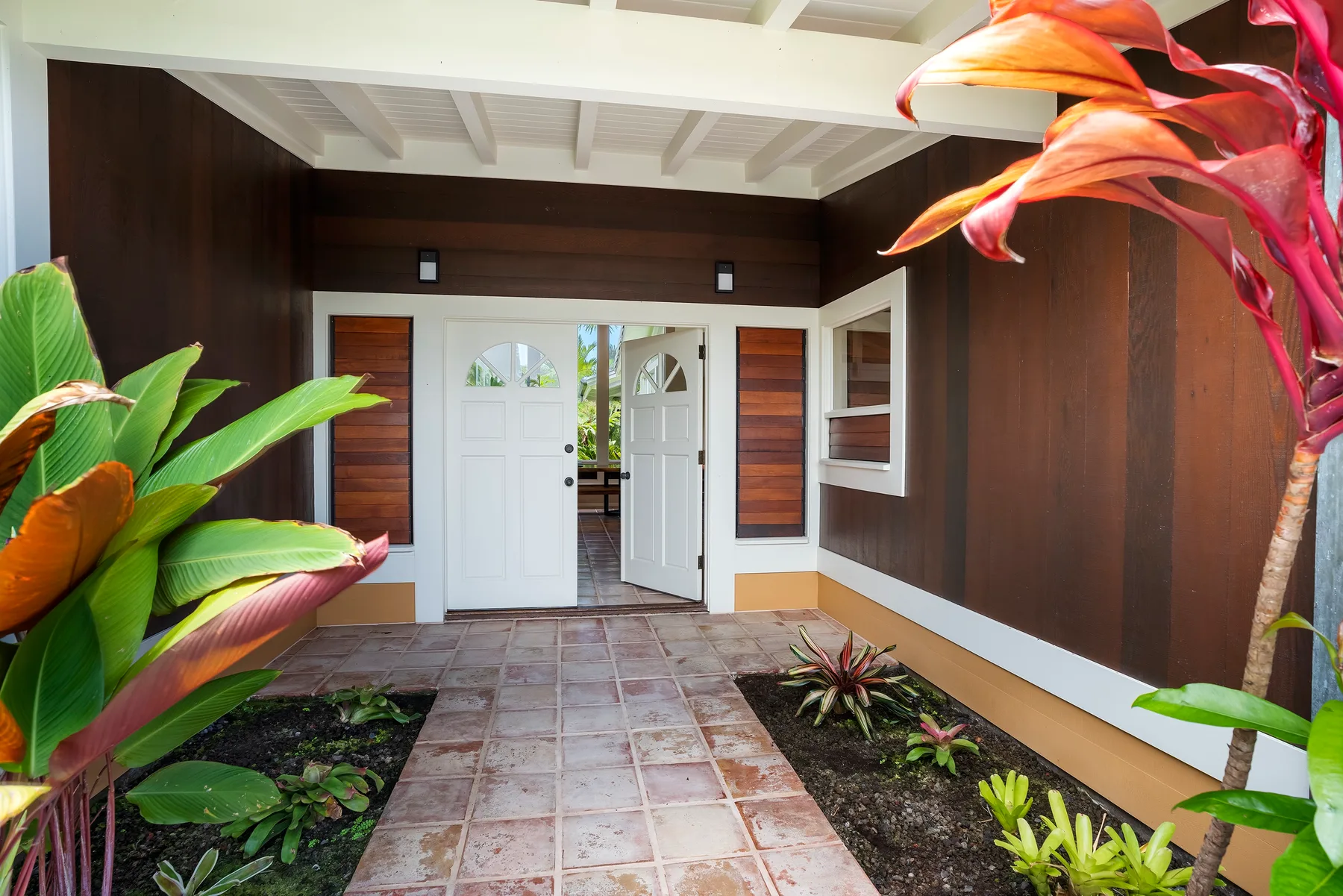 Una entrada cubierta con puertas dobles blancas y parterres con plantas.