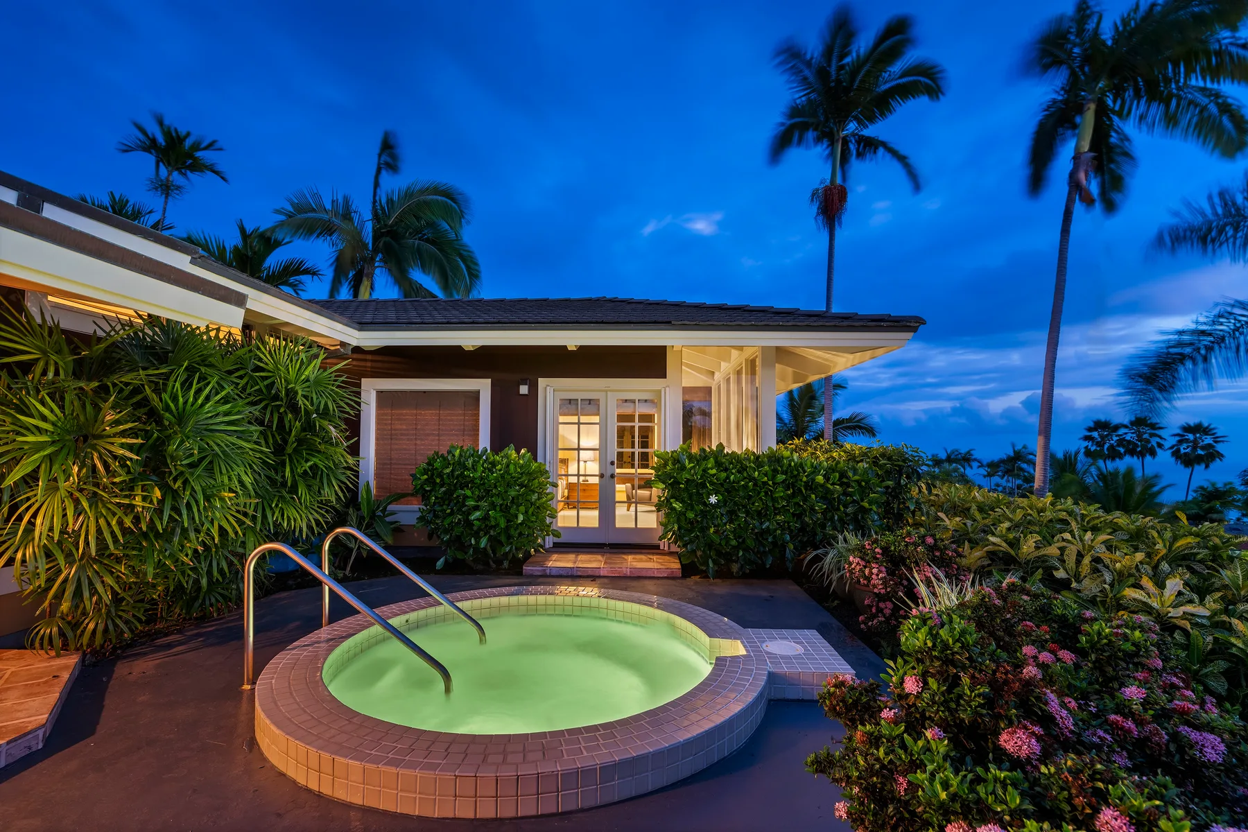 Una pequeña piscina exterior está junto a una casa moderna rodeada de plantas tropicales.