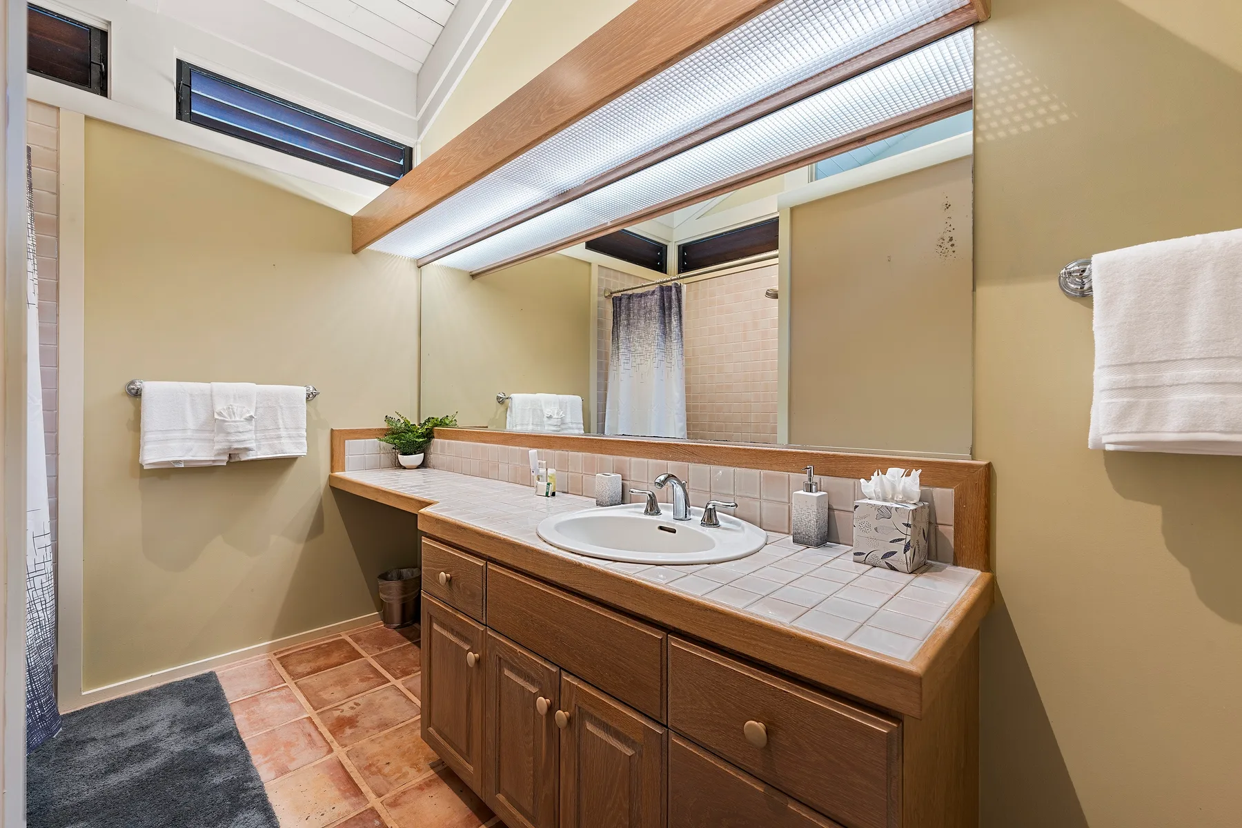 Un mueble de baño con lavabo está bajo un espejo grande y luces superiores.