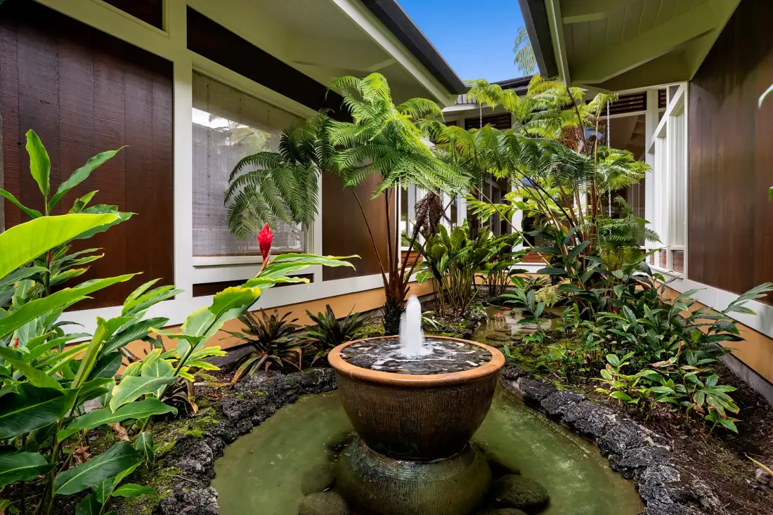 Un frondoso patio interior tiene plantas tropicales alrededor de una pequeña fuente.