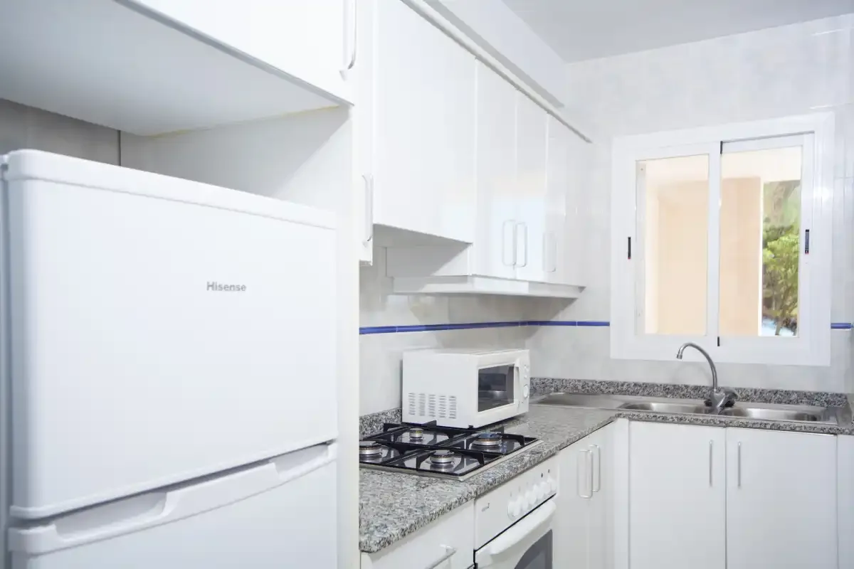 Una cocina luminosa con armarios blancos, un refrigerador y una cocina de gas.