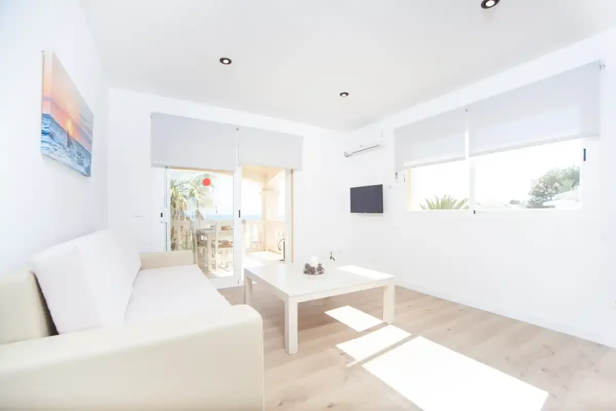 Una sala de estar luminosa con asientos, una mesa de centro y ventanas grandes.