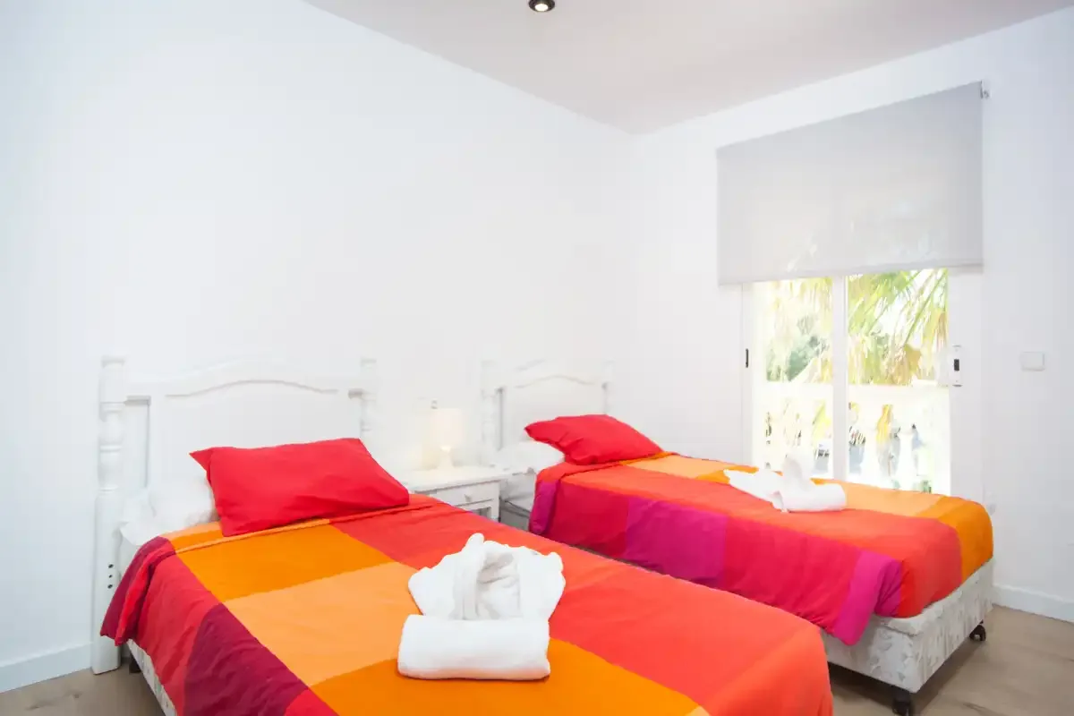 Un dormitorio luminoso con dos camas vestidas con ropa de cama roja y naranja.
