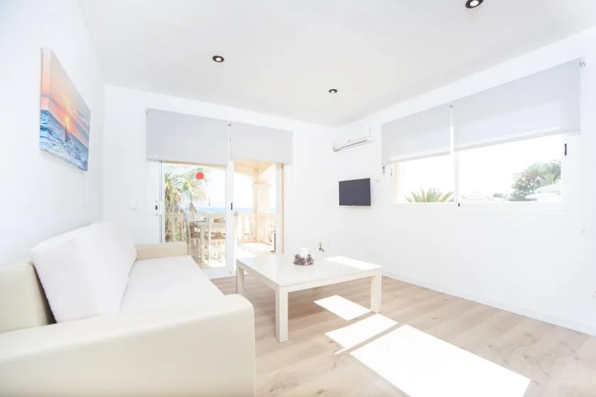 Una sala luminosa con asientos blancos, una mesa baja y ventanas grandes.