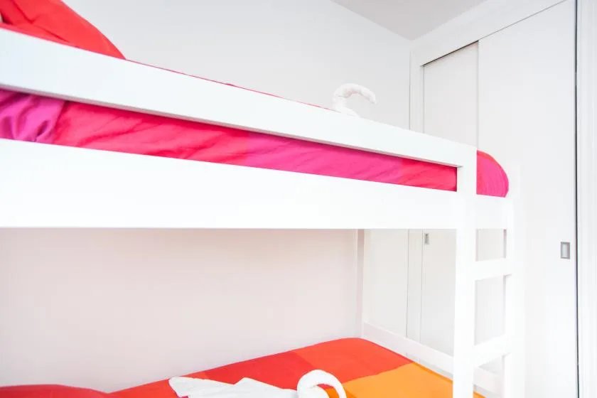 Un dormitorio luminoso con una litera blanca y ropa de cama rosa y naranja.