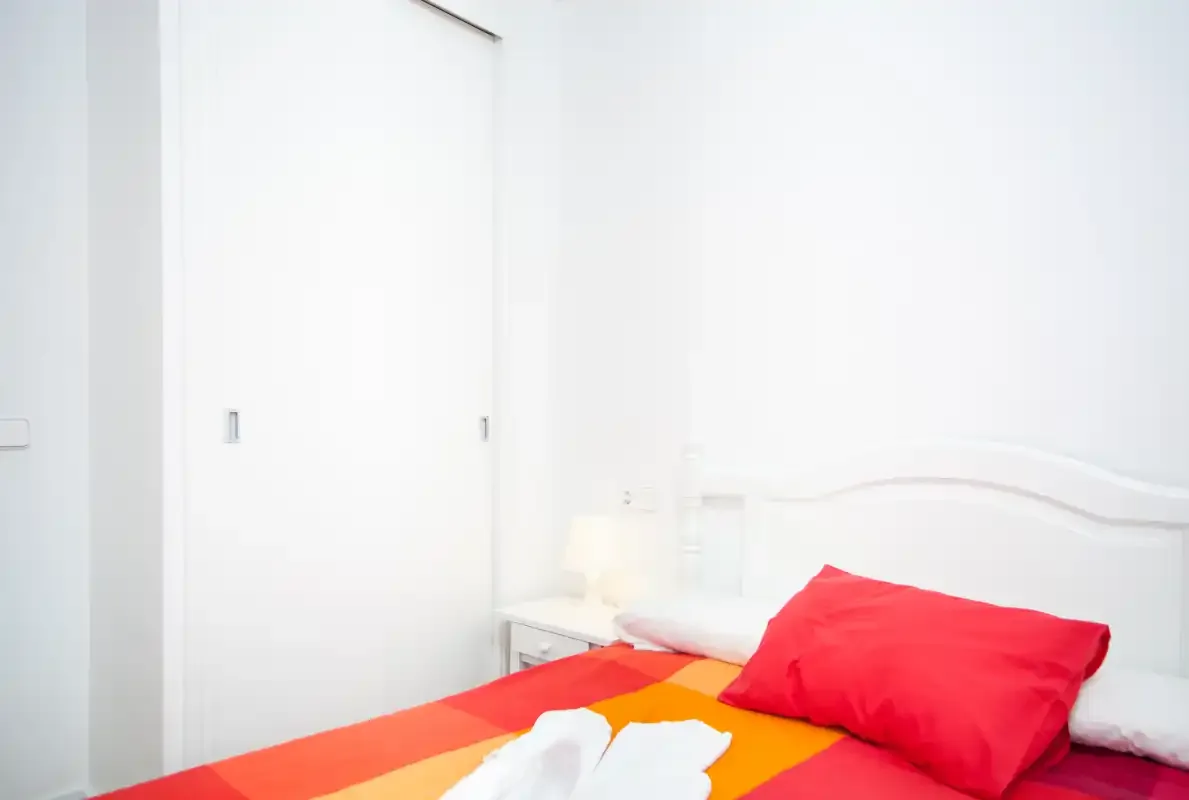 Un dormitorio con una cama vestida con ropa de cama roja y naranja brillante.