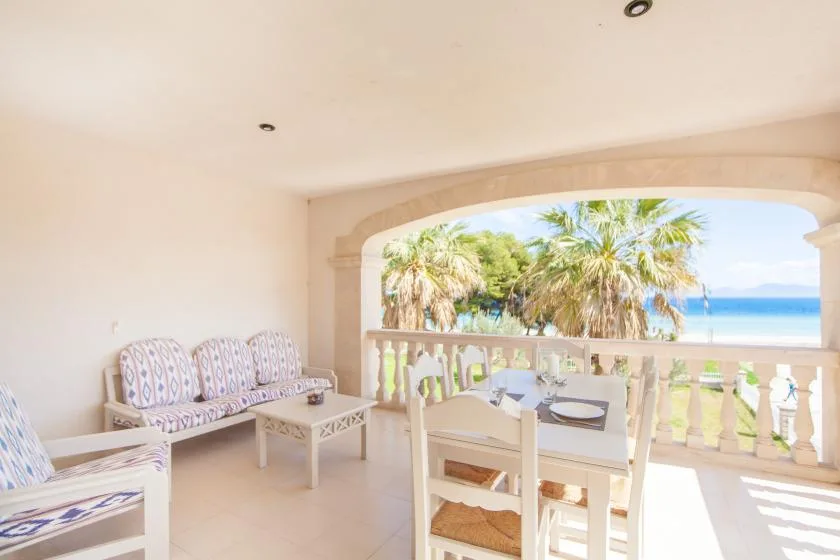 Una terraza cubierta tiene asientos estampados y una mesa de comedor con vistas a palmeras y al mar.