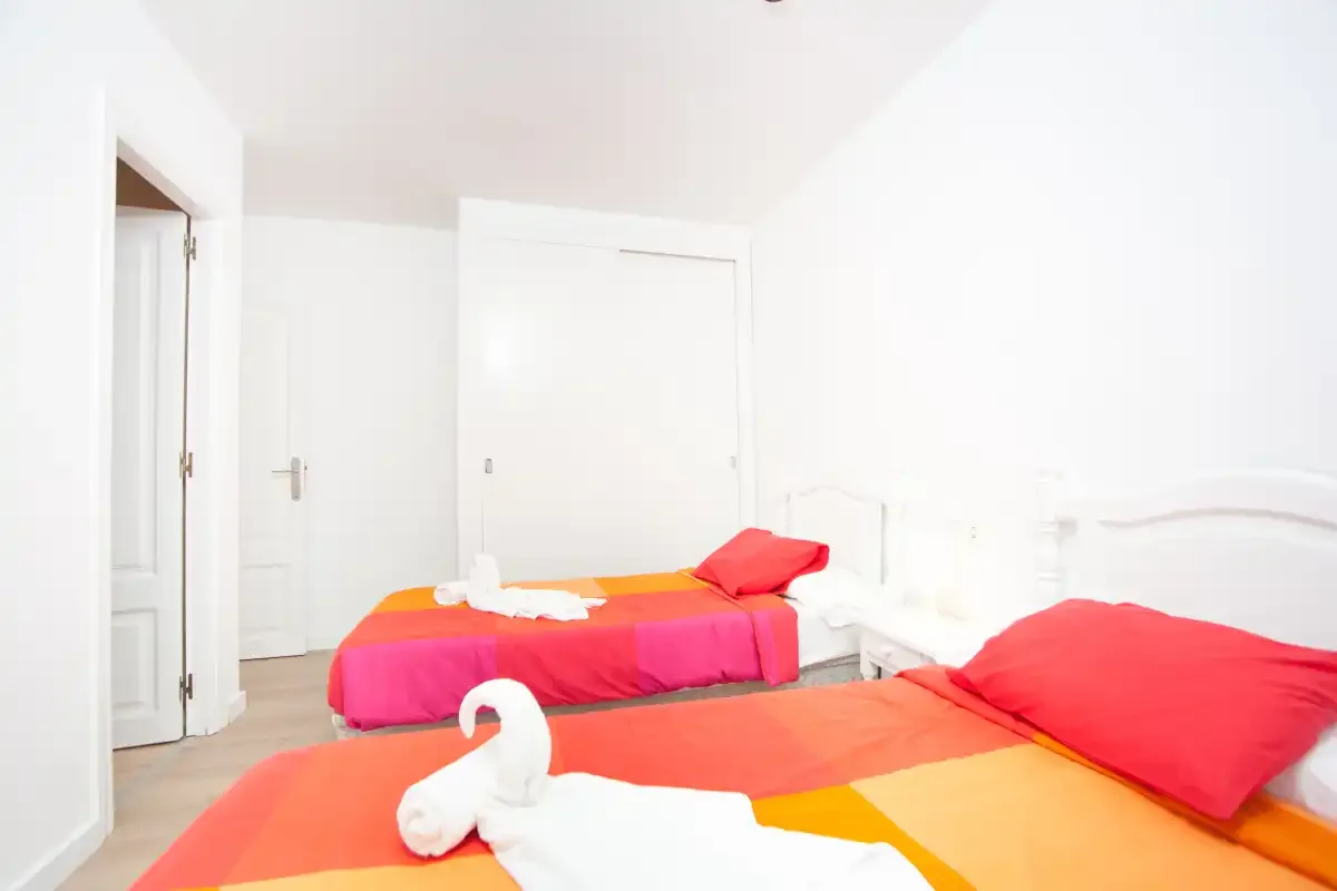 Un dormitorio luminoso con dos camas vestidas con ropa de cama naranja y rosa.