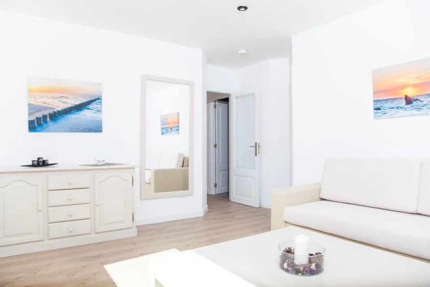 Una luminosa sala de estar blanca con un sofá y una imagen costera enmarcada.