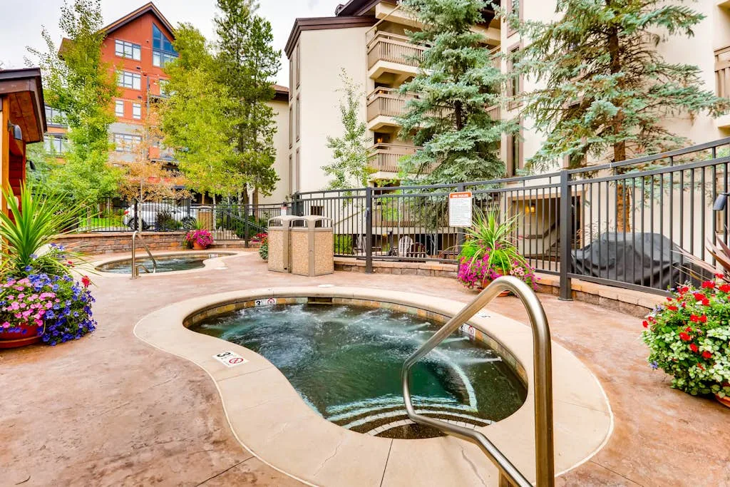 Una bañera de hidromasaje al aire libre está en un patio ajardinado junto a edificios de apartamentos.