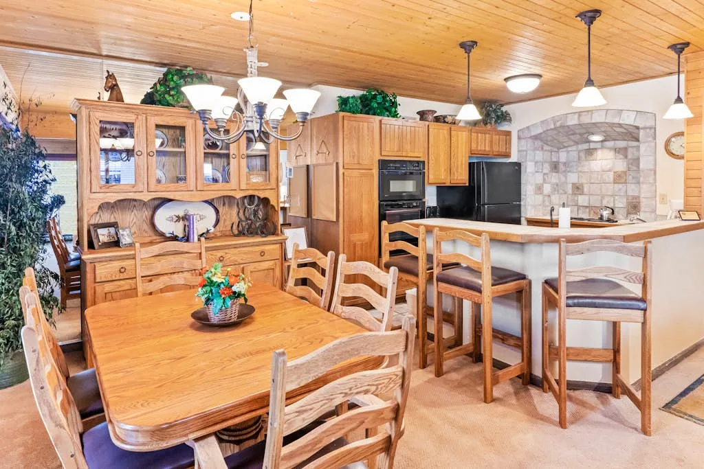 Un comedor amueblado en madera da a una cocina con barra para desayunar.