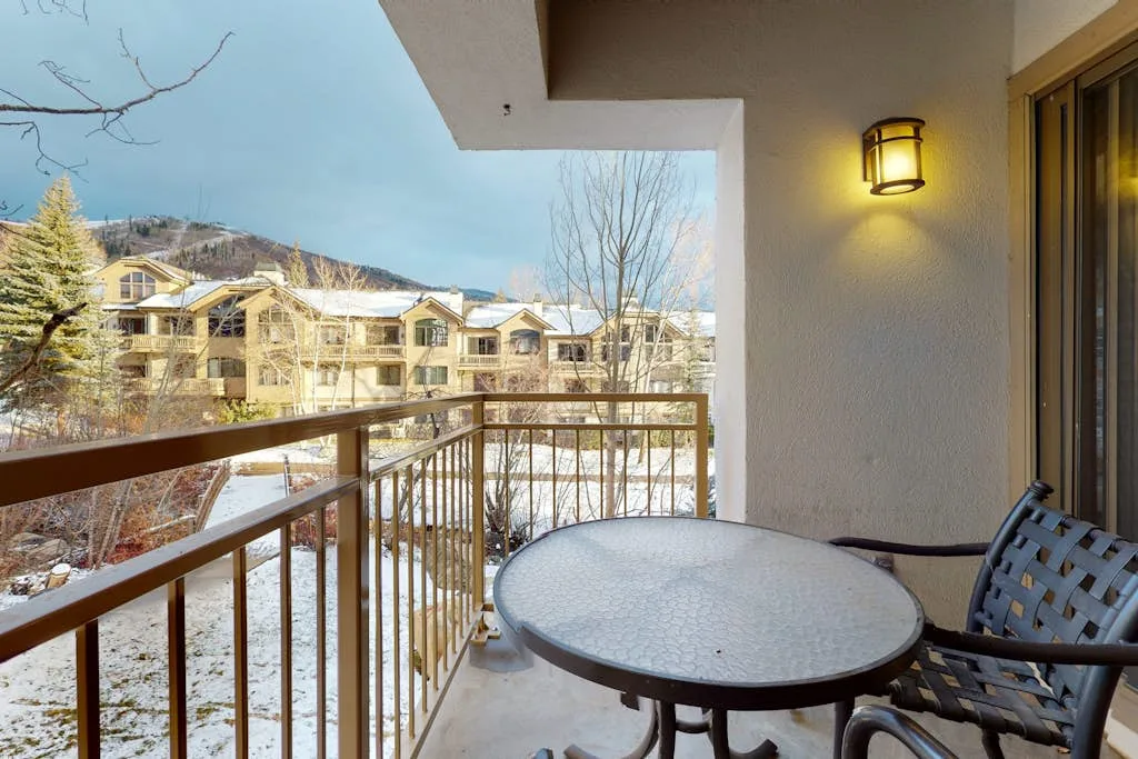 A covered balcony has a round table and seating overlooking snow-covered grounds.
