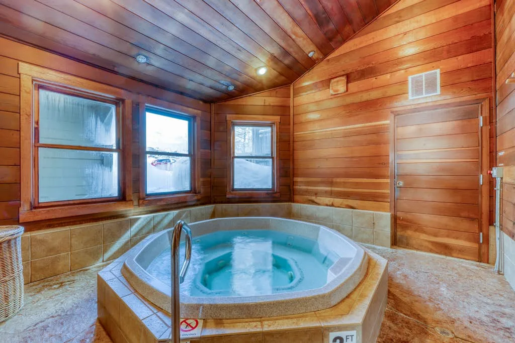 A hot tub sits in a wood-paneled room with windows.