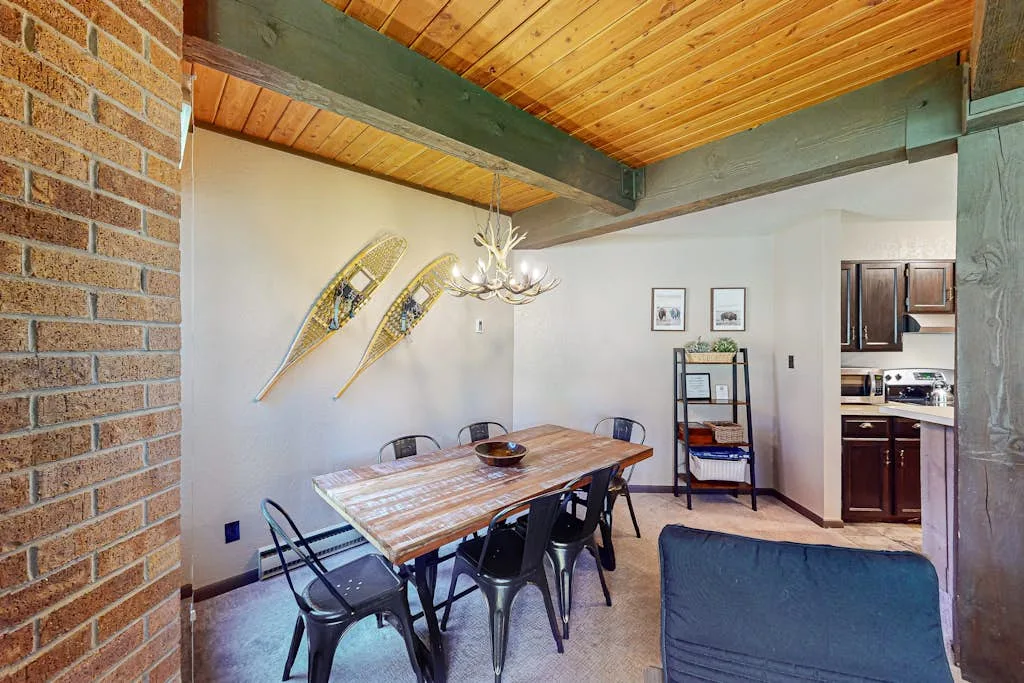 A dining area with a wooden table and chairs beneath a timber ceiling.