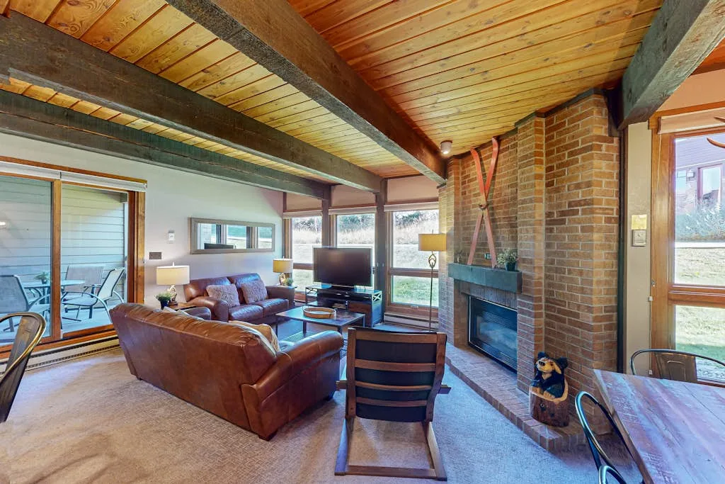 A living room with exposed wooden beams, seating, and a brick fireplace.