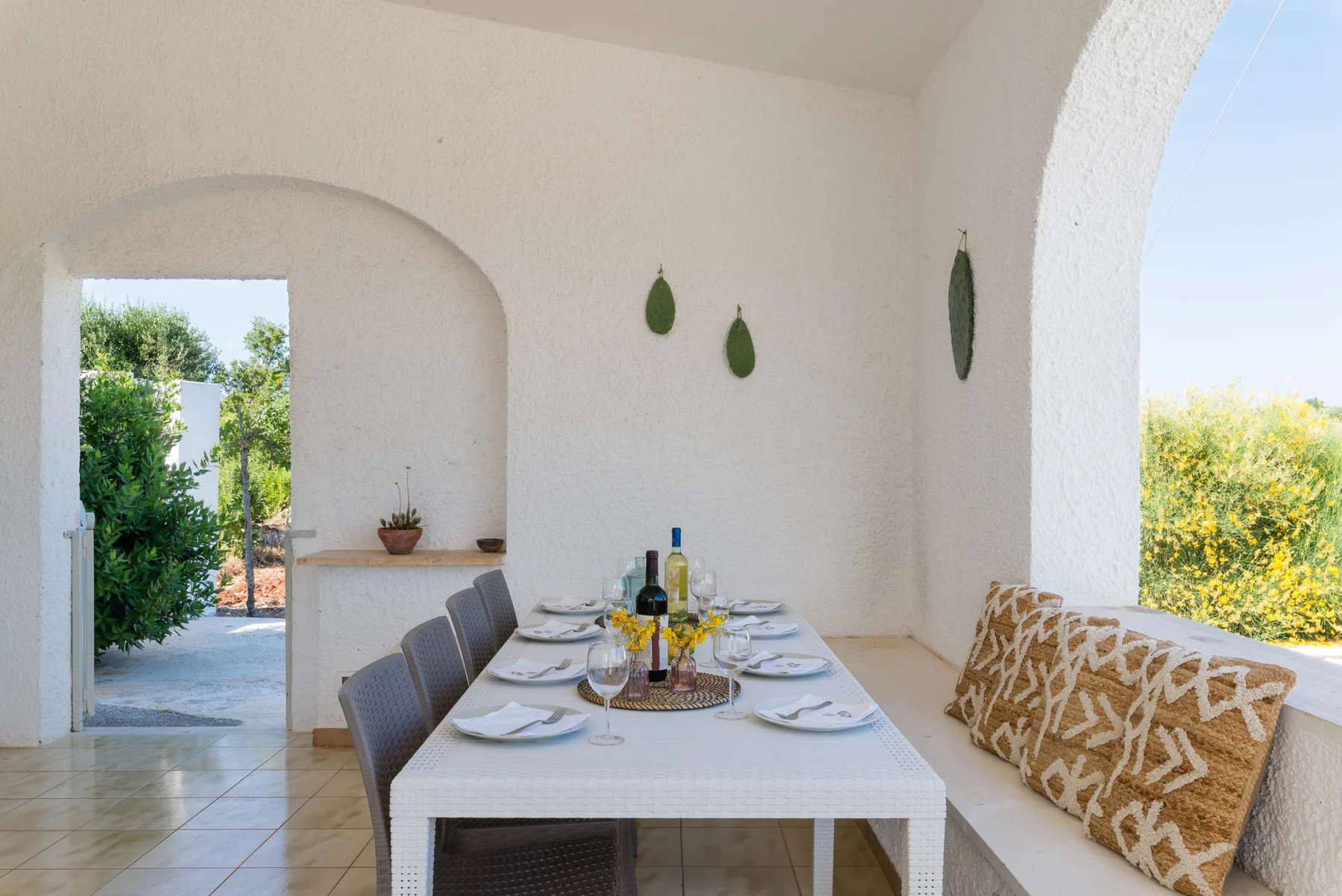 A bright dining area with a set table beside an arched opening to greenery.
