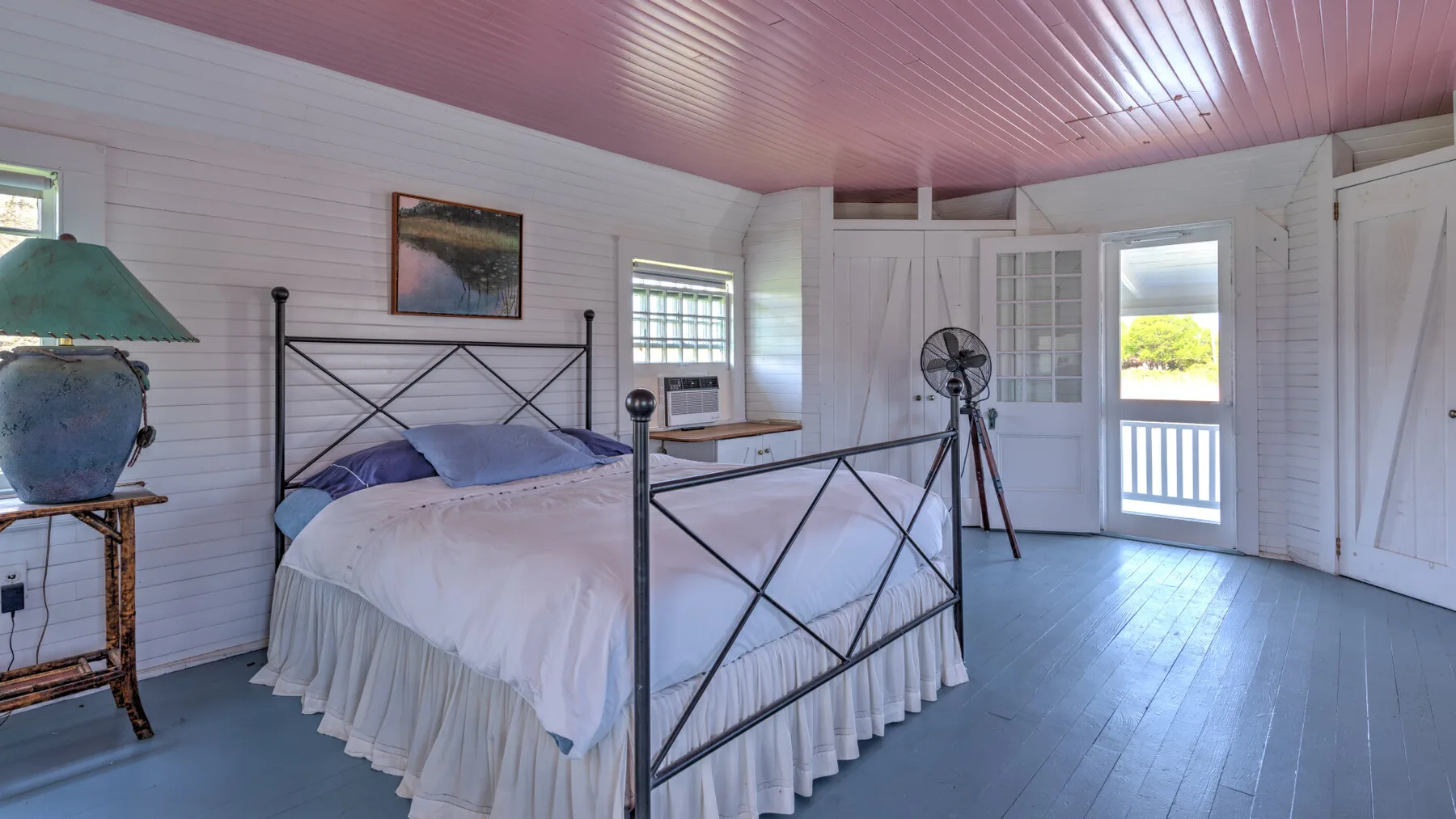 Un dormitorio luminoso con una cama, paredes blancas y una puerta de balcón abierta.