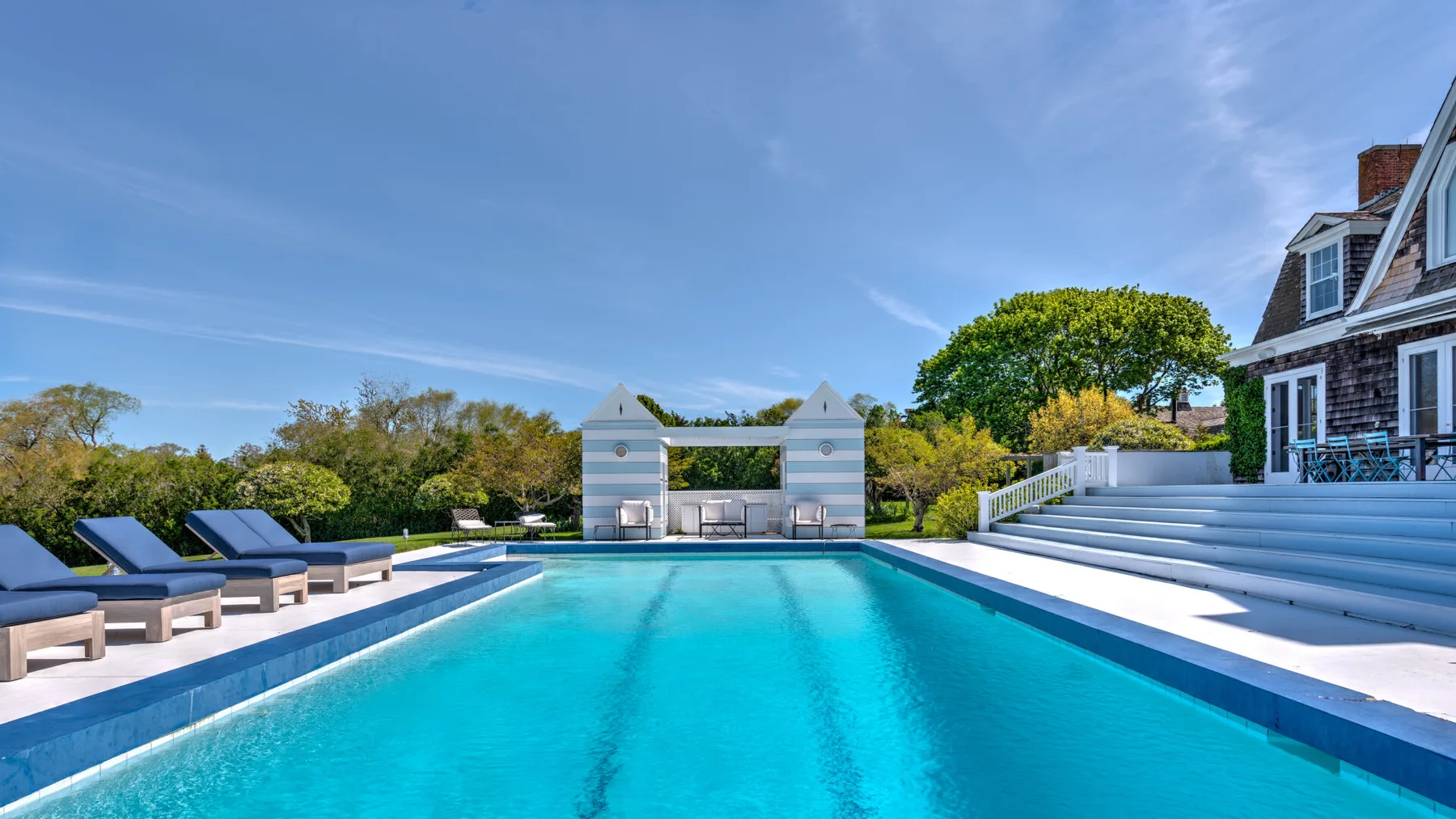 Piscina al aire libre con asientos para descansar y una escalera blanca junto a la casa.