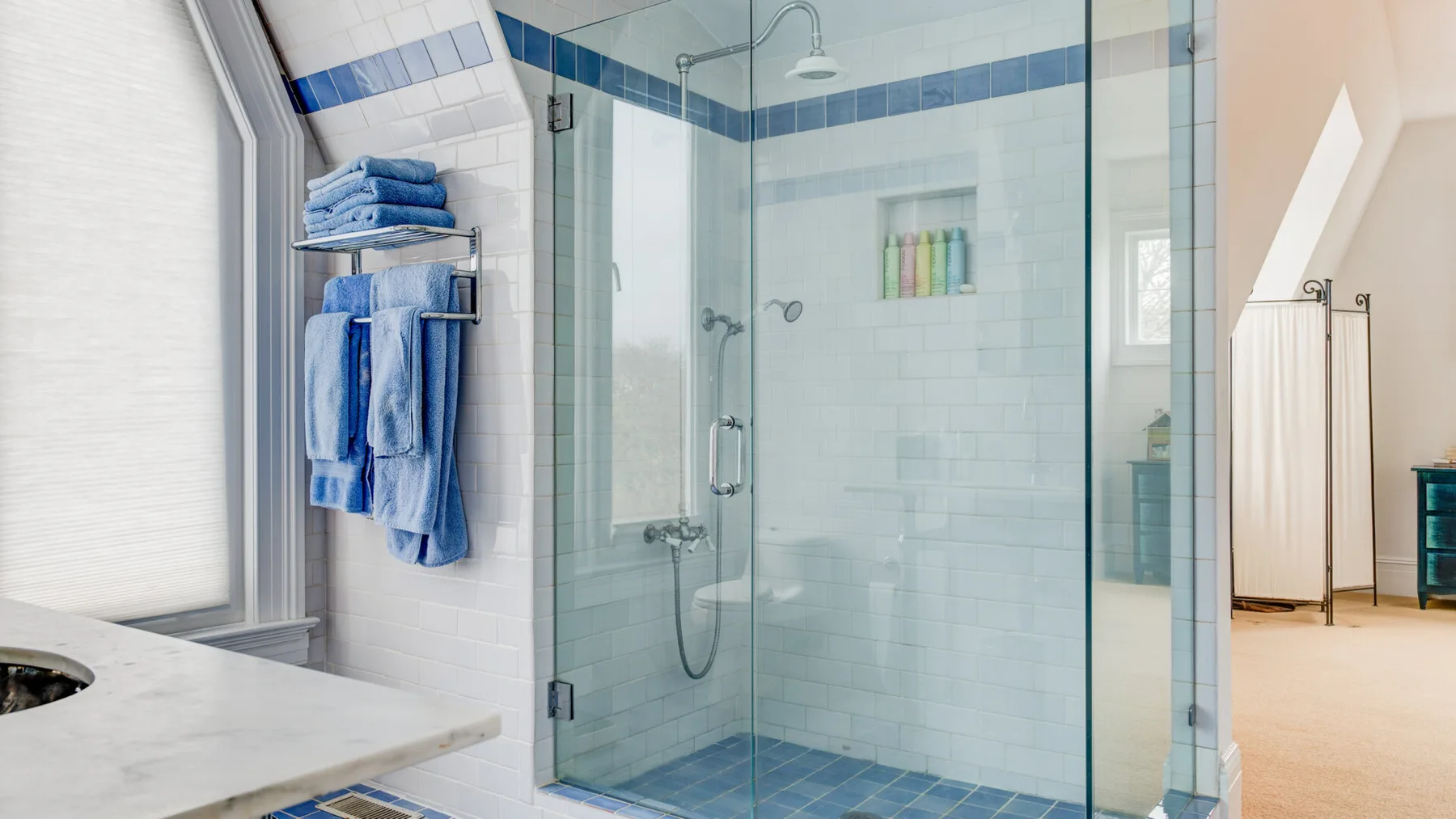 Un baño con azulejos, una ducha de vidrio y toallas azules dobladas.