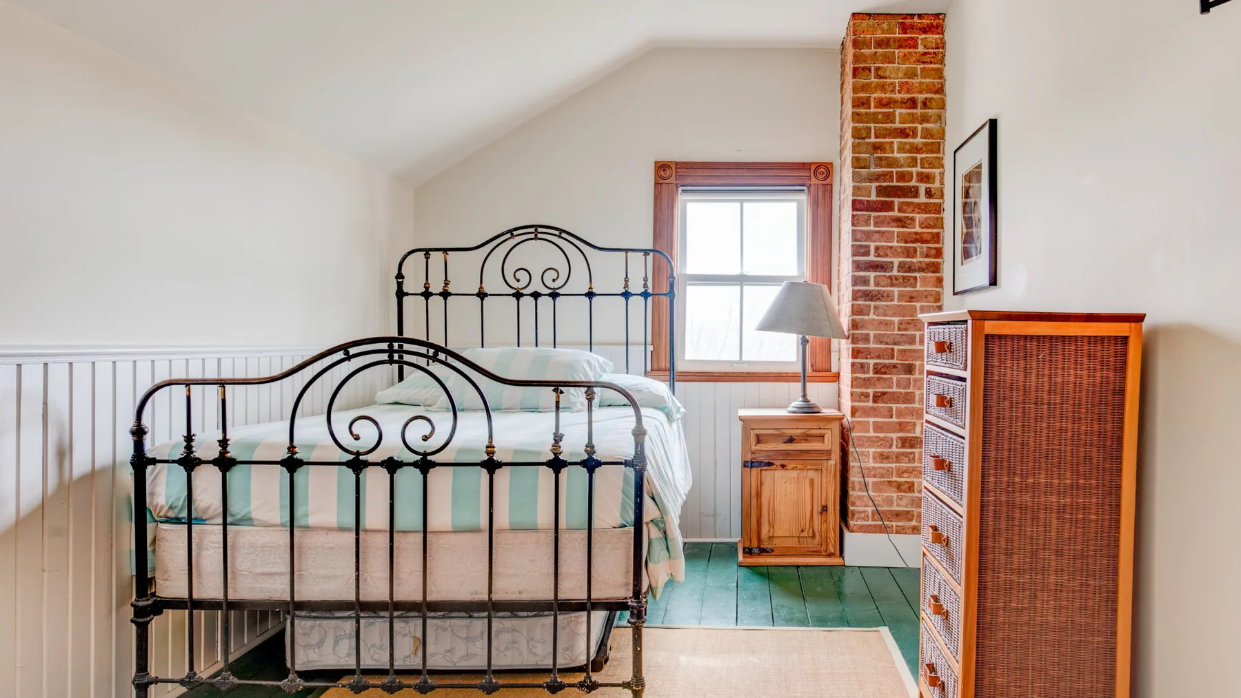 Un dormitorio luminoso con una cama de metal, una ventana y muebles de madera.