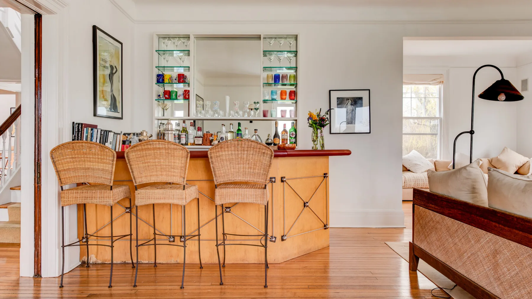 Un bar en una casa luminosa con asientos de mimbre y estantes con botellas.