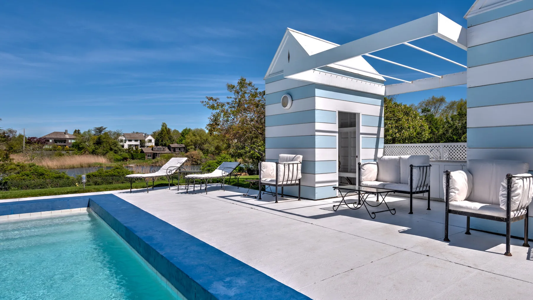 Una piscina exterior junto a un patio embaldosado con asientos y un edificio a rayas.