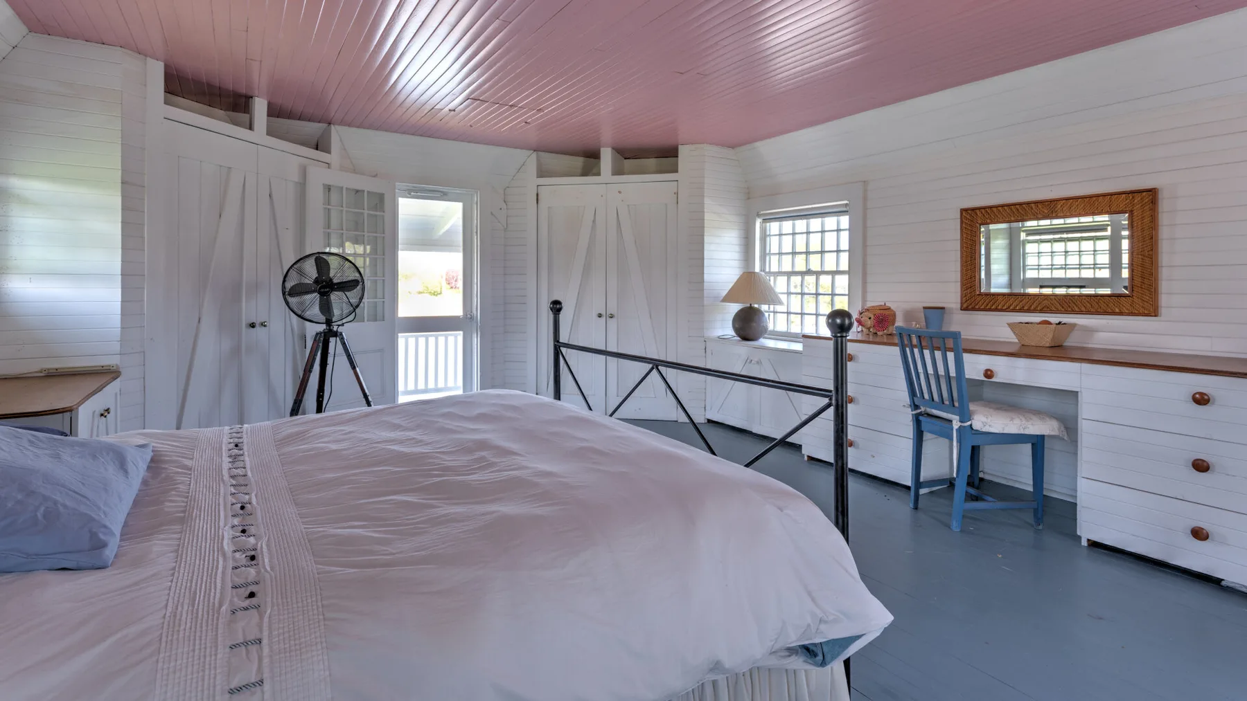 Un dormitorio luminoso con una cama, una silla azul y ventanas a lo largo de la pared.