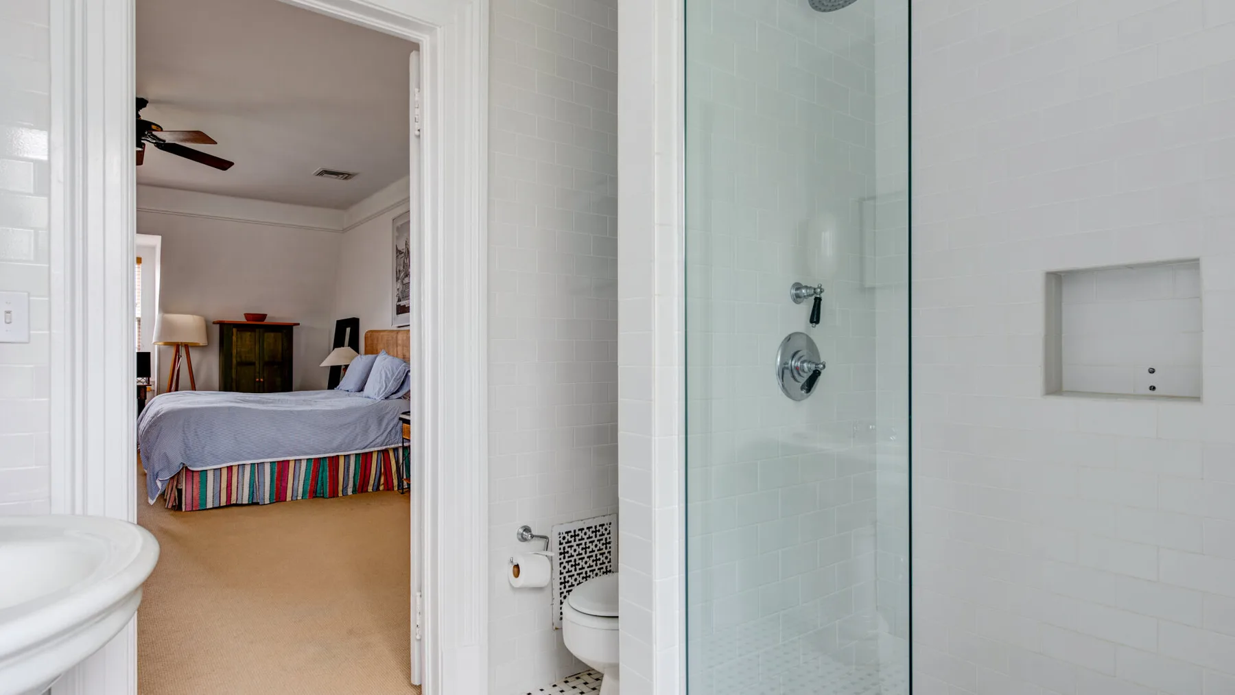 Un baño con una ducha de vidrio y vista a un dormitorio.