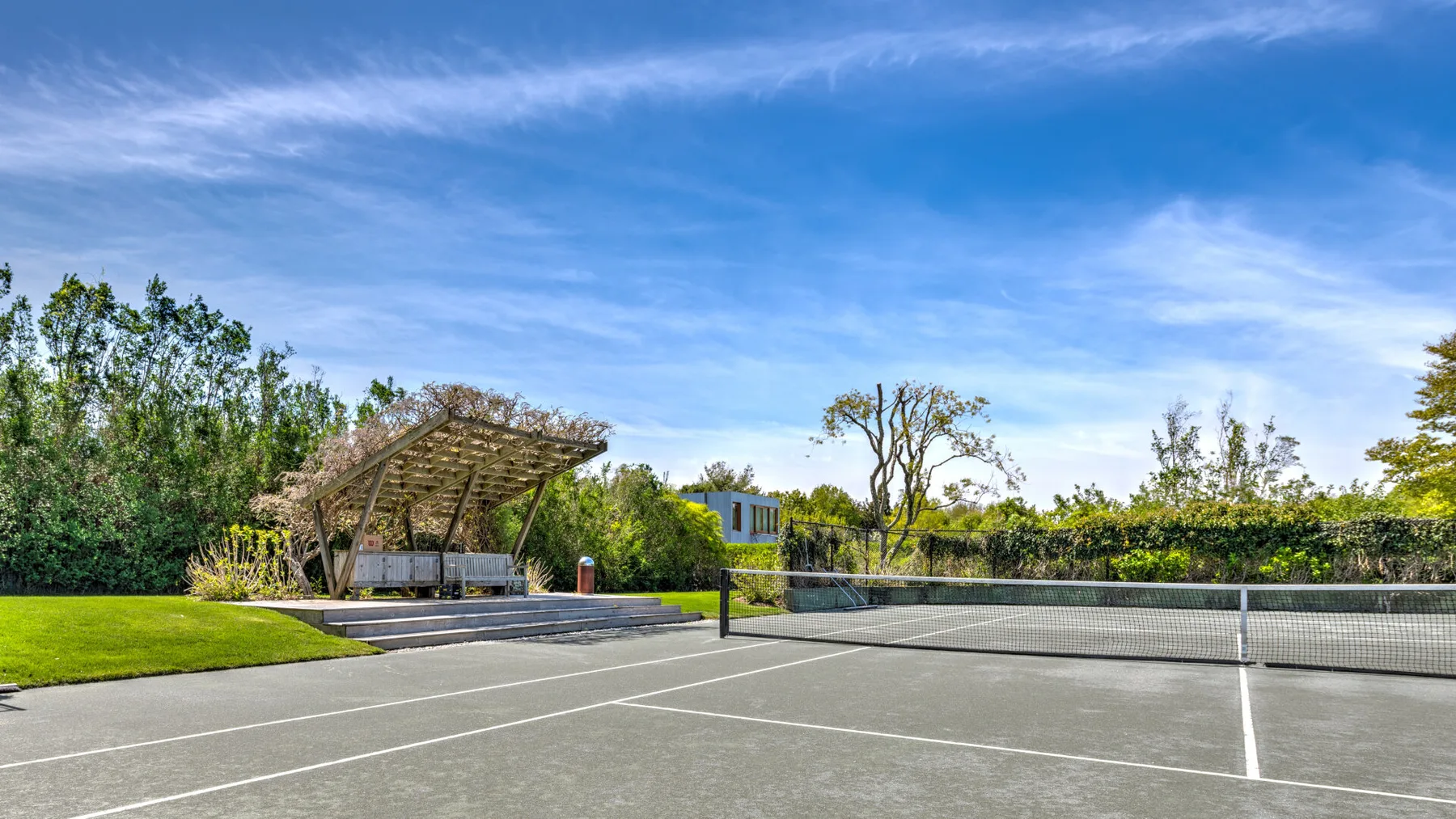 Cancha de tenis al aire libre con una red y una zona de asientos a la sombra.