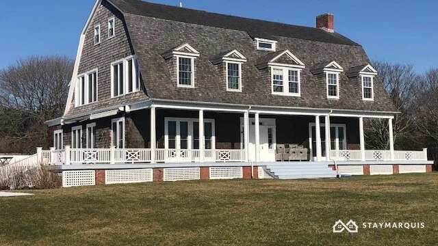 Una casa grande con un amplio porche blanco se alza junto a un césped abierto.