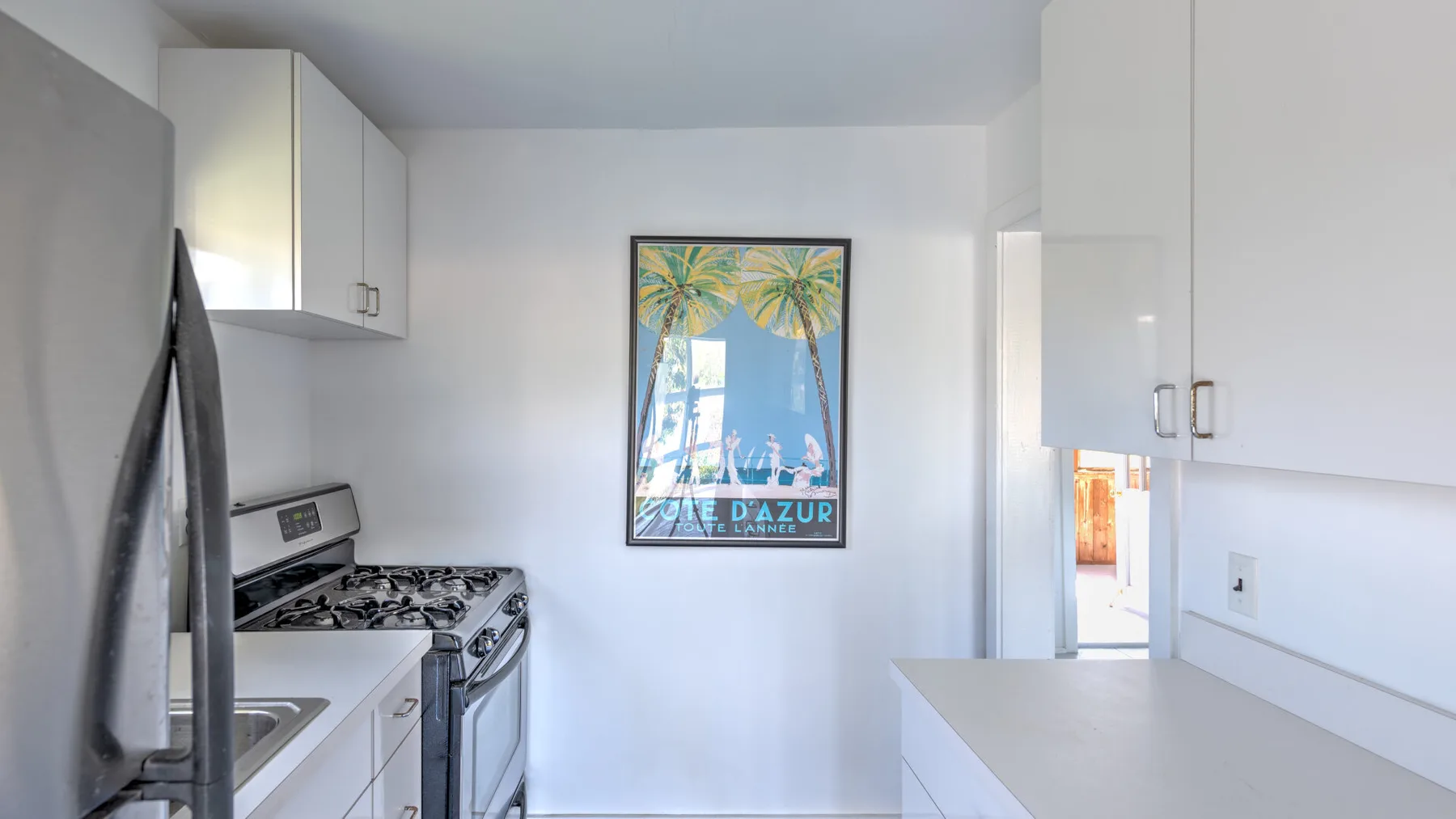 Una cocina luminosa con gabinetes blancos, una estufa y un póster tropical enmarcado.
