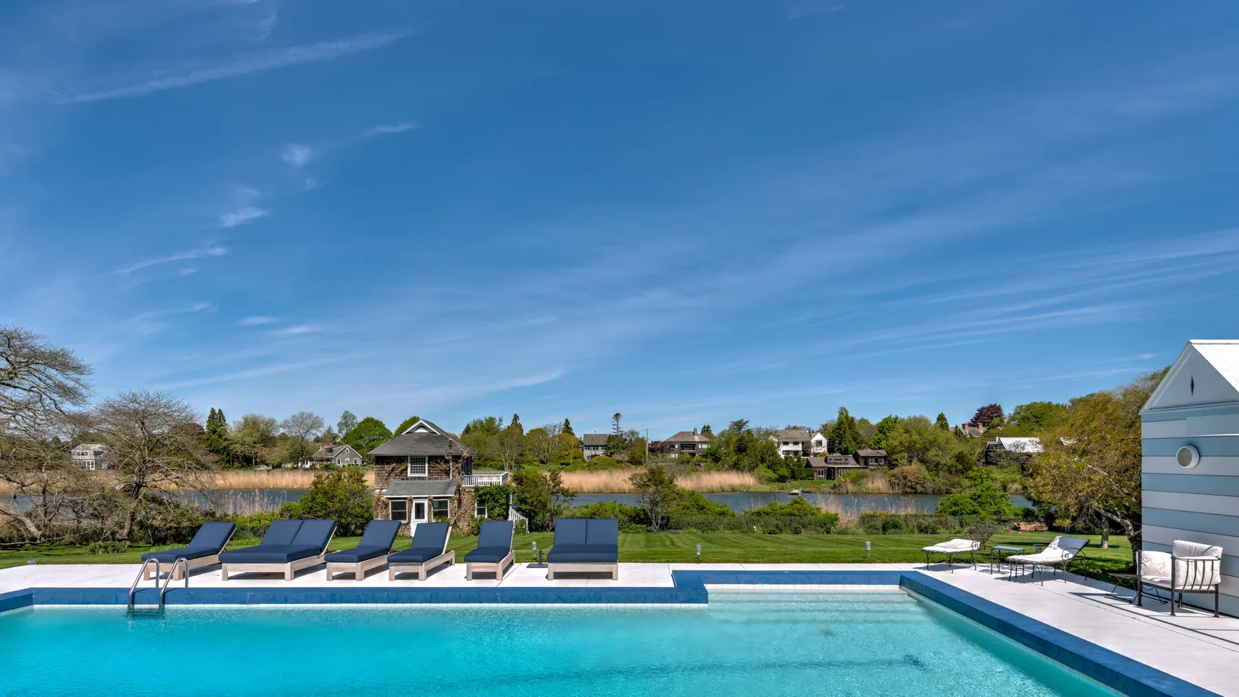 Una piscina junto a un paisaje junto al lago y asientos al aire libre.